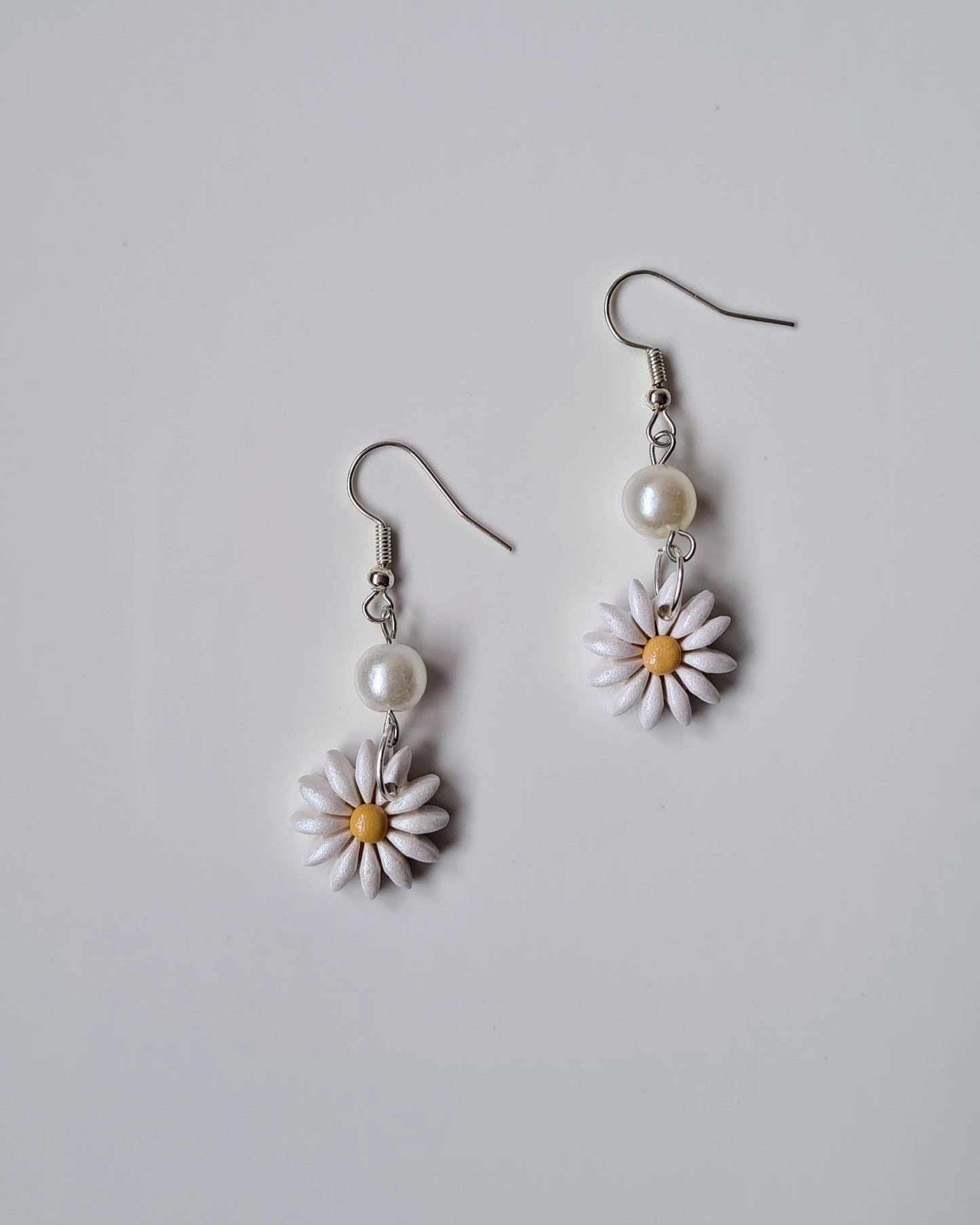 Pair of daisy flower earrings with pearl accents on a light gray background