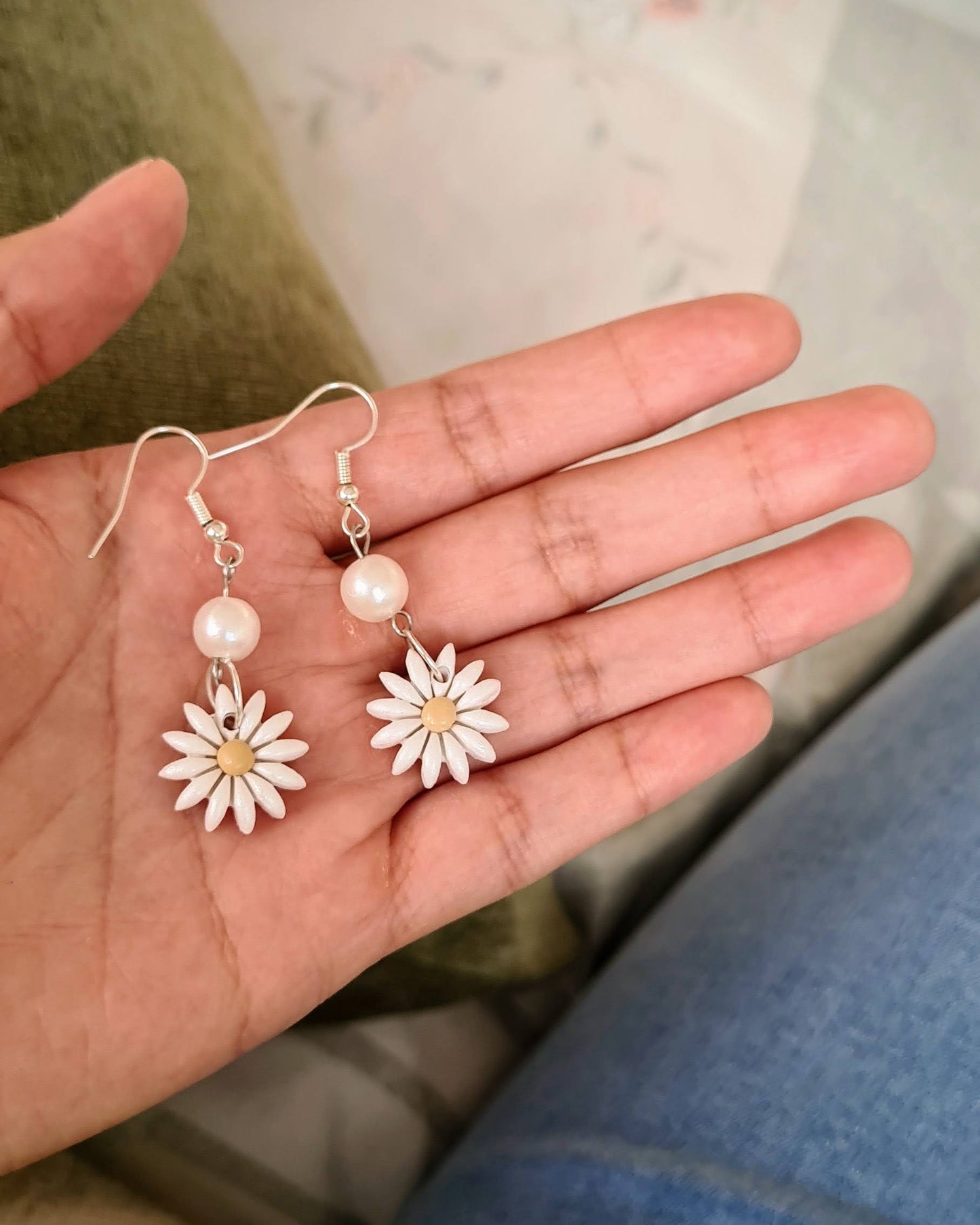 Hand holding a set of floral earrings with a light background