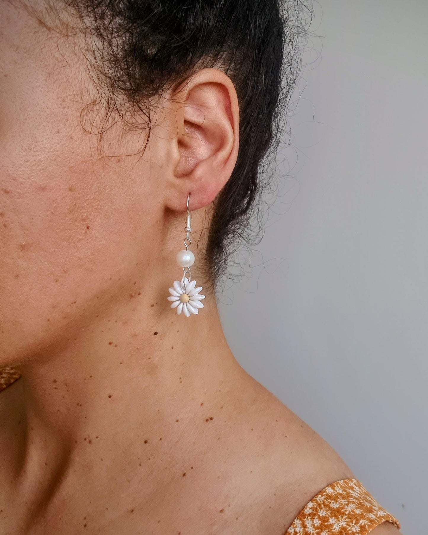 Close-up of a person wearing a floral earring with a plain background