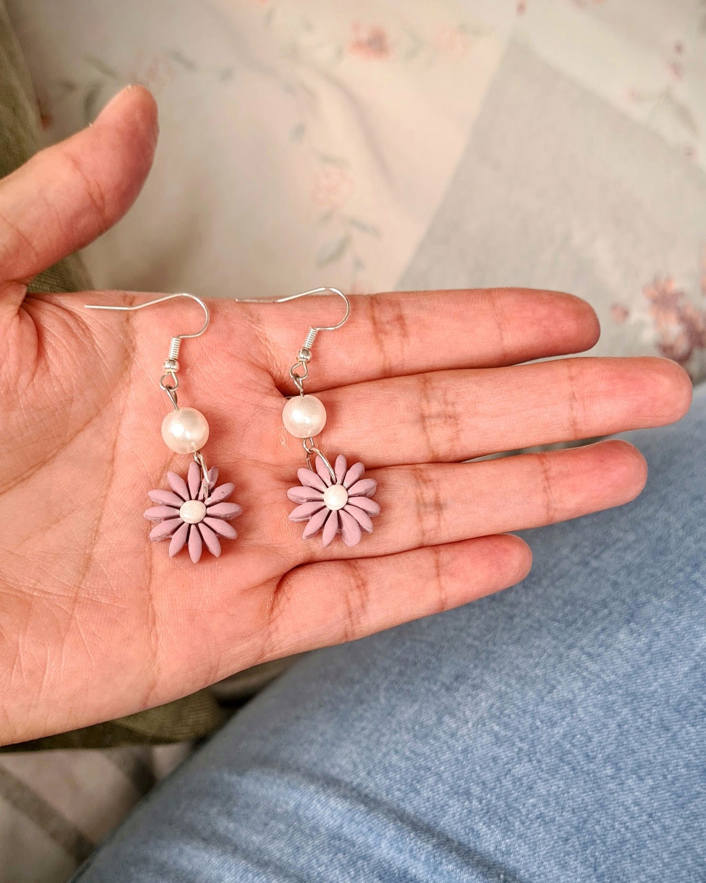 Hand holding pair of earrings with a floral design on a light background