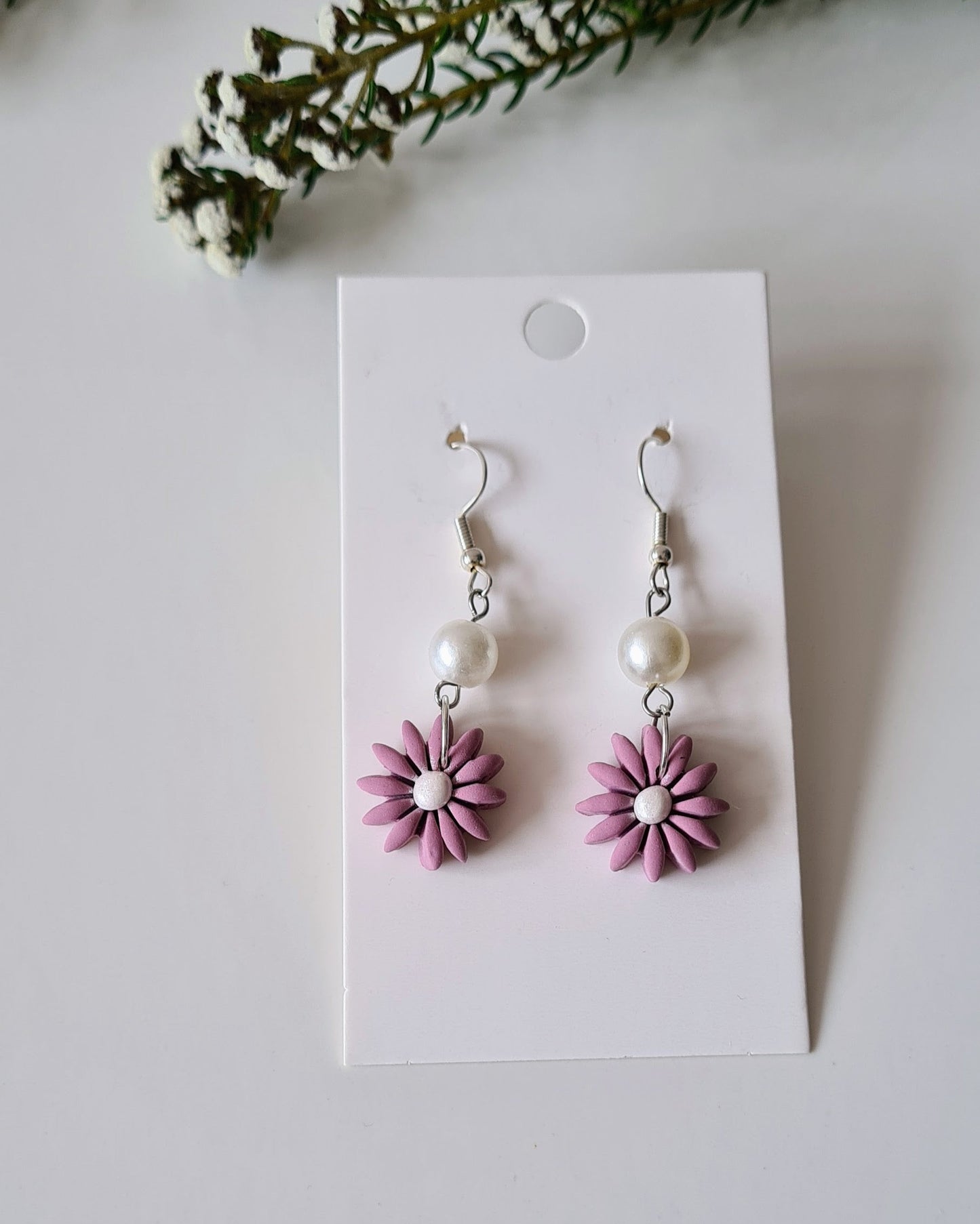Pair of Lavender flower-shaped earrings on a white card with greenery around.