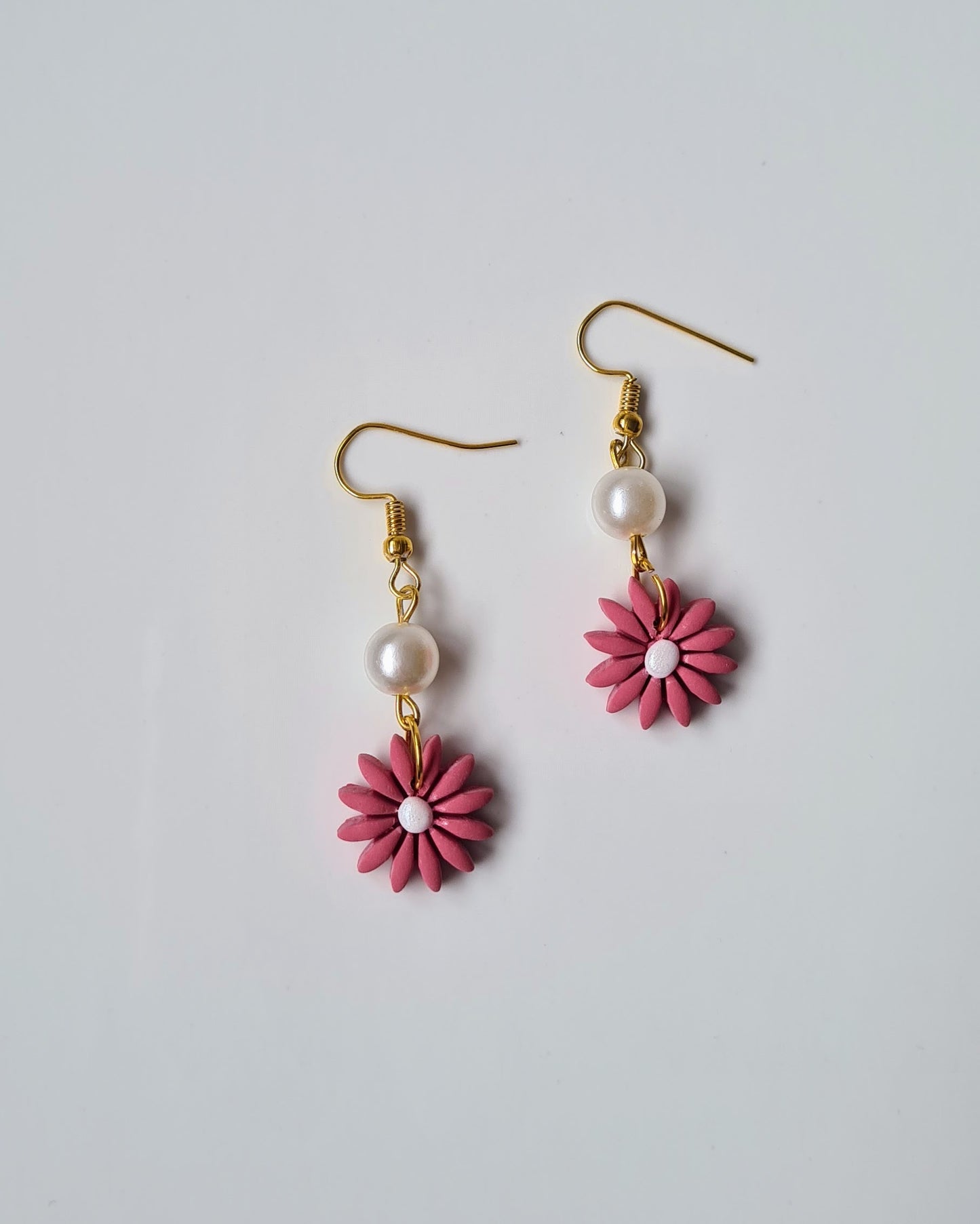 Pair of pink flower-shaped earrings with pearl centers on a light gray background
