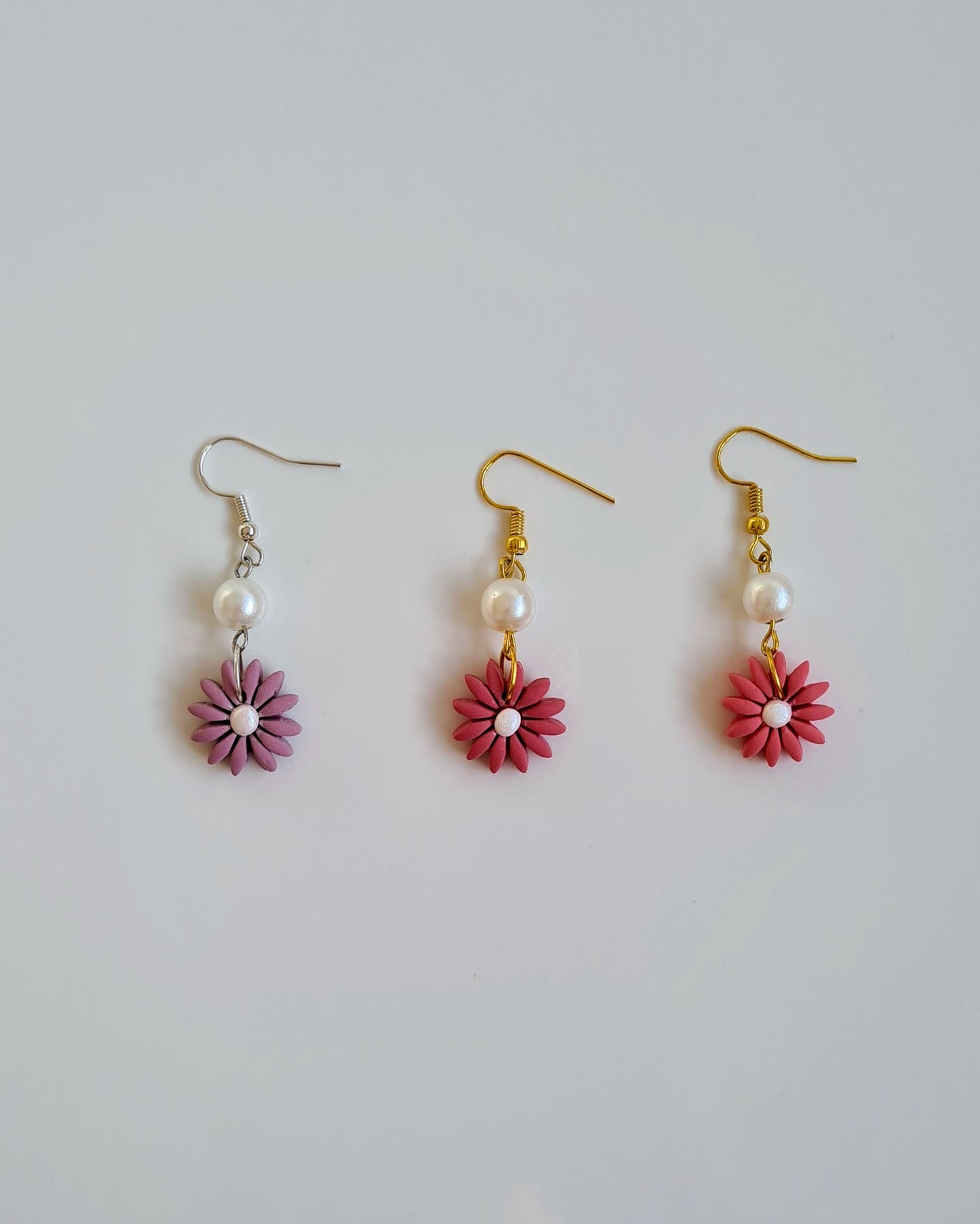 Three pairs of earrings with pink flowers and pearls on a light gray background