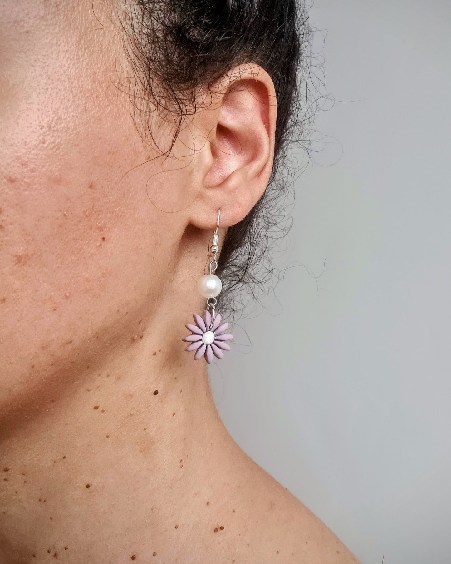Close-up of an ear wearing a floral earring with a pearl center against a neutral background
