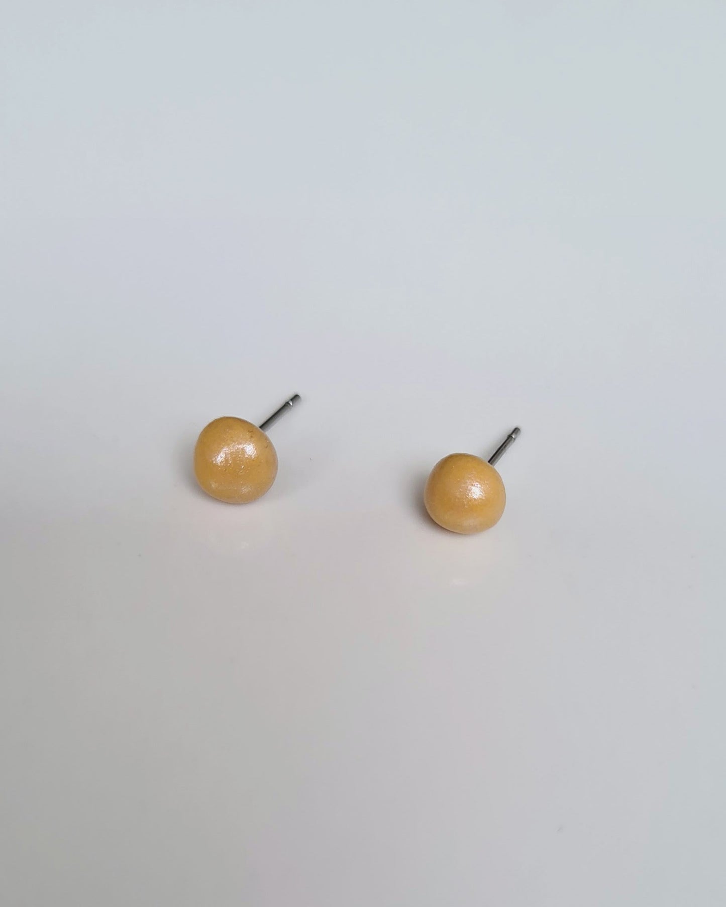 Mustard coloured pearlescent studs on a grey background