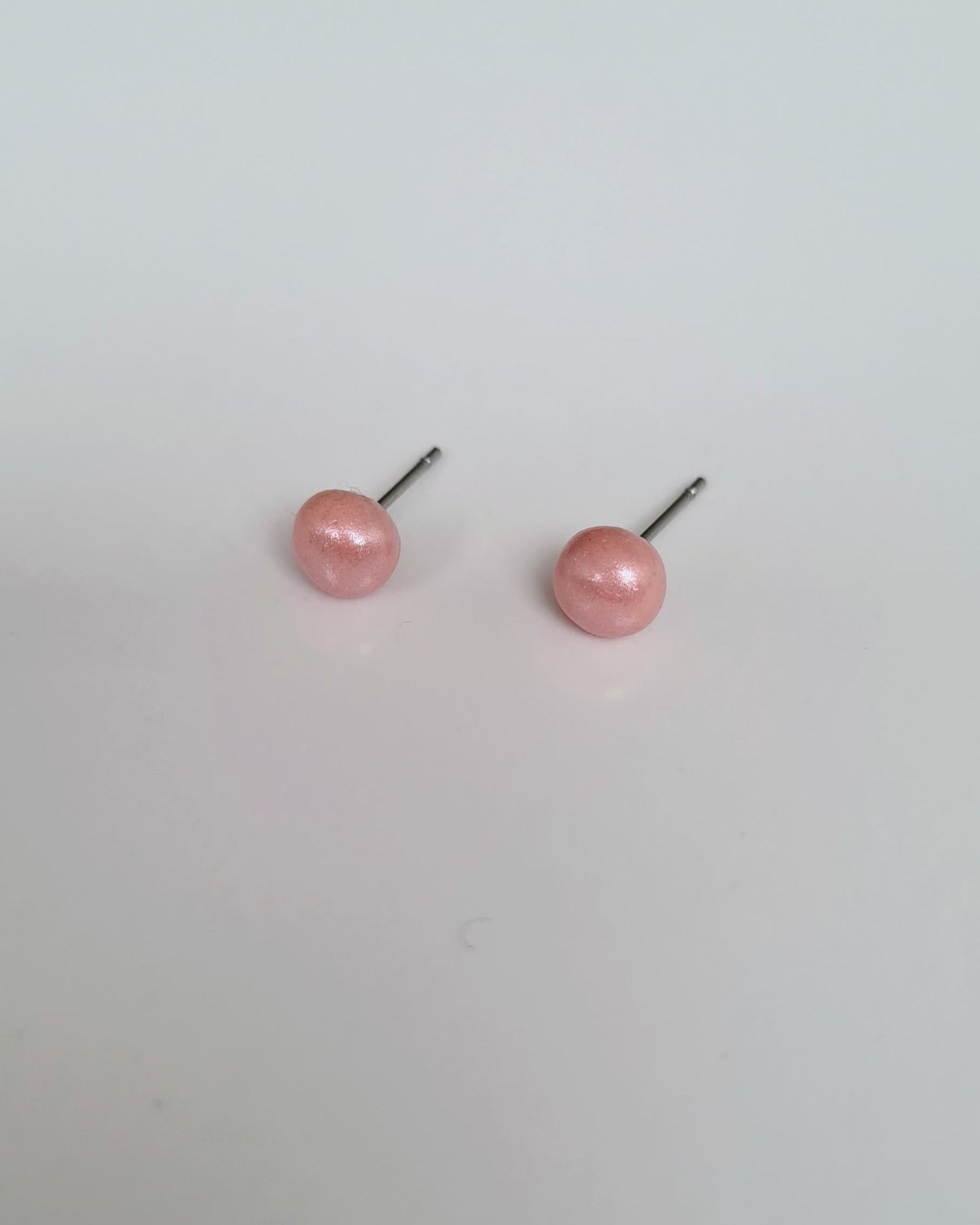 Pair of peach coloured pearl earrings on a light grey background