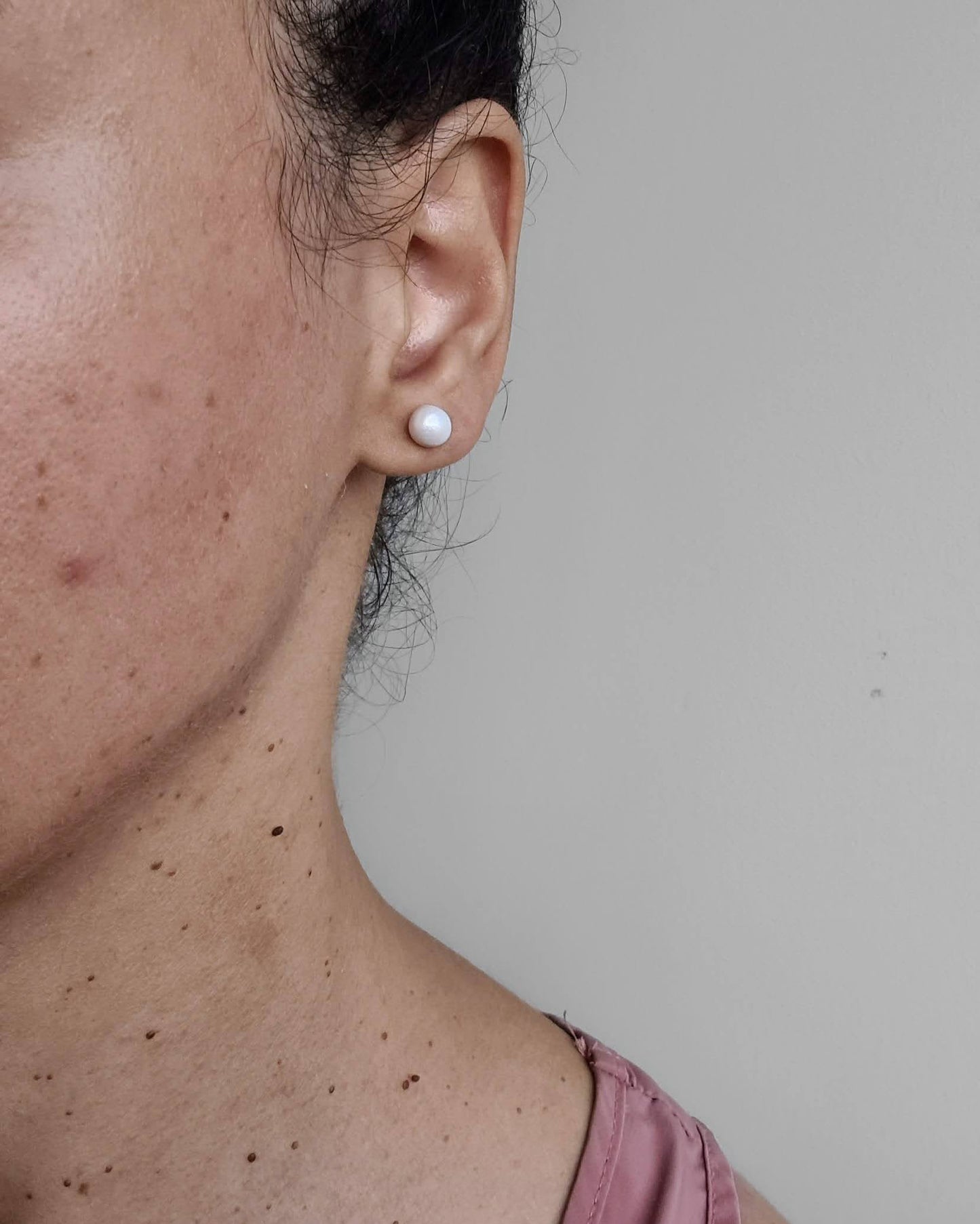 Close-up of a person wearing a pearl earring against a plain background