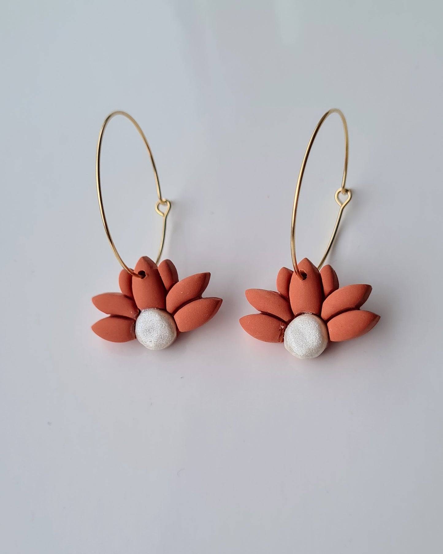 Pair of cinnamon coloured flower-shaped hoop earrings with pearl centres on a light grey background