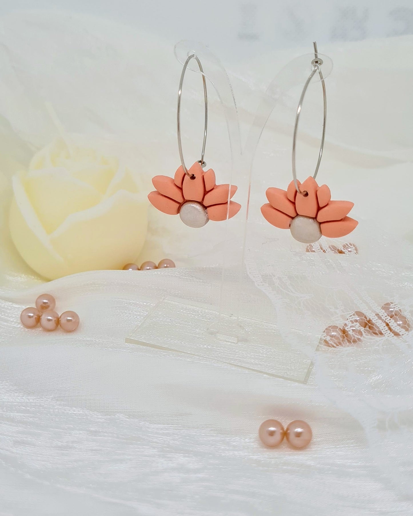 Floral hoop earrings on transparent stand on a satin white surface with a blurred background