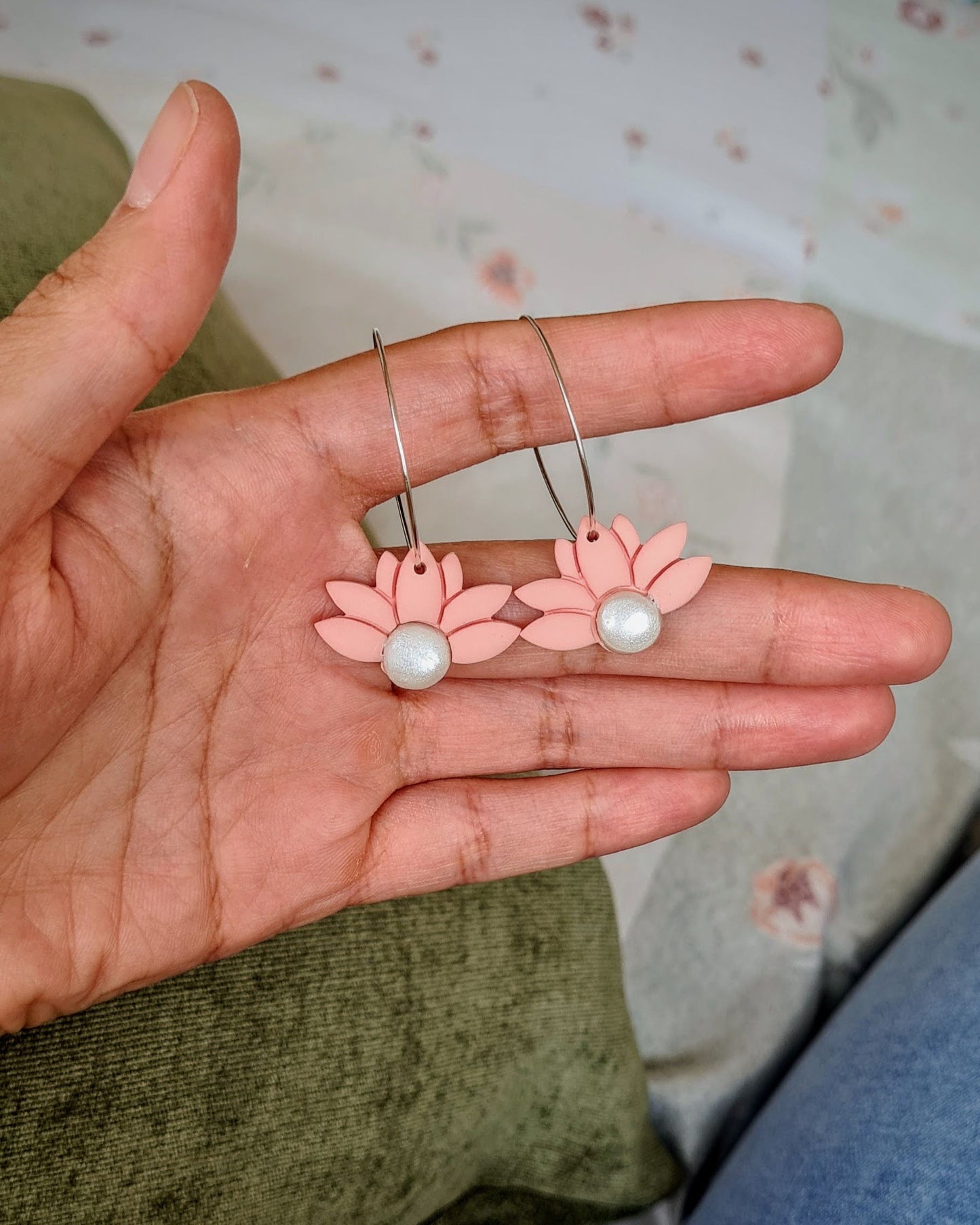 Hand holding peach coloured floral hoop earrings with pearl centres against a floral patterned background