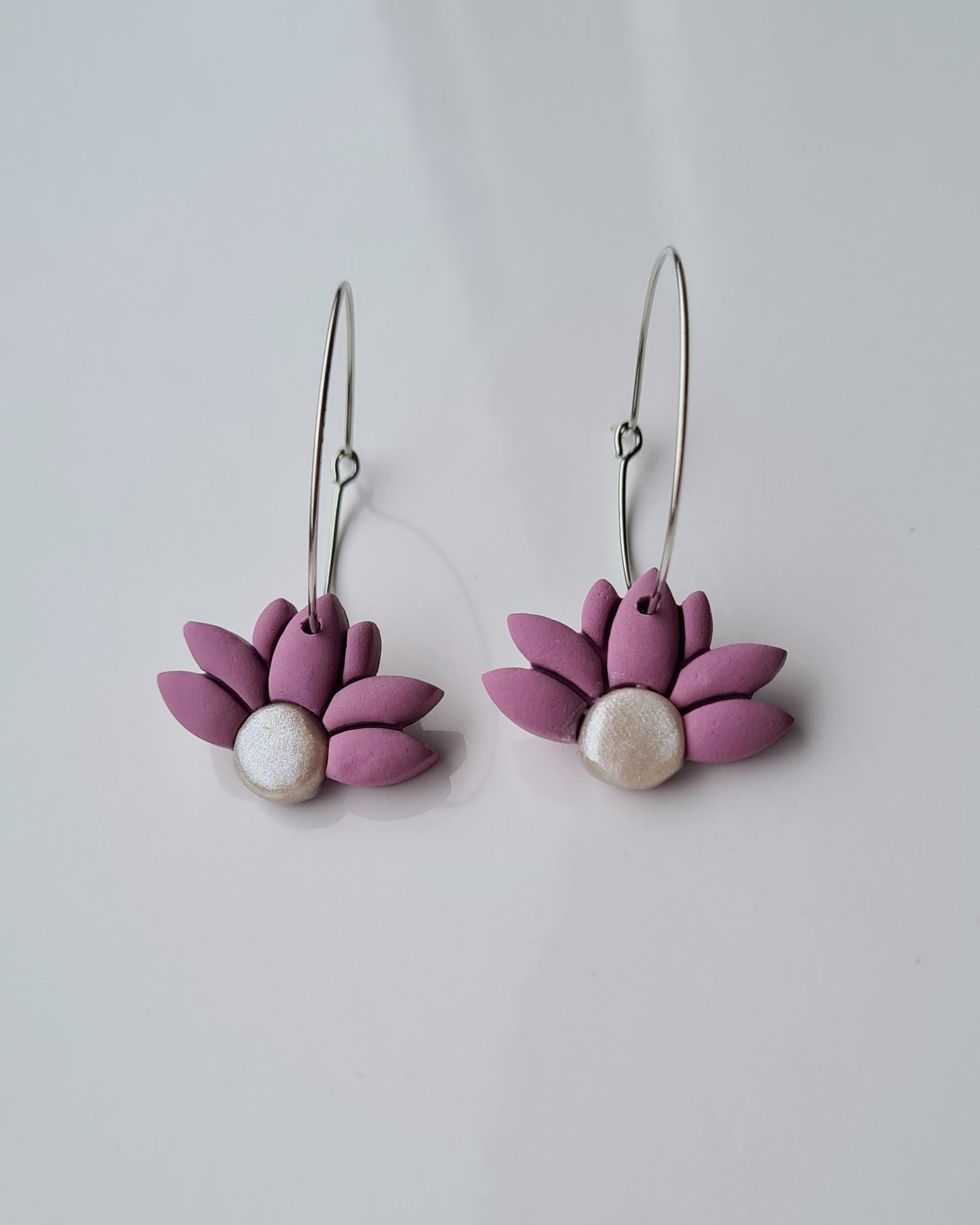 Pair of lavender coloured flower-shaped hoop earrings with pearl centres on a light grey background