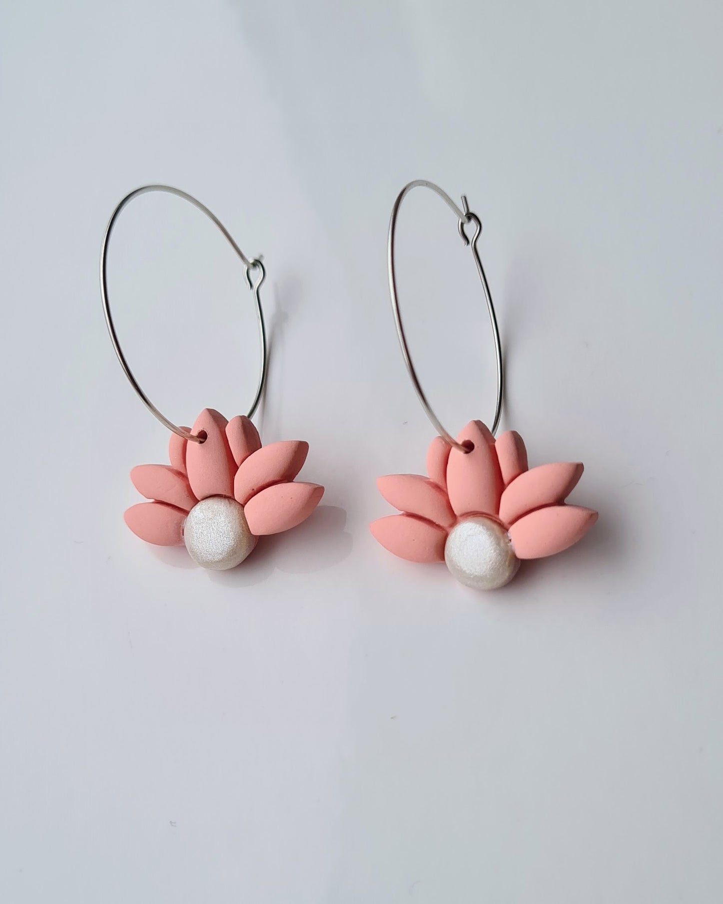 Pair of peach coloured flower-shaped hoop earrings with pearl centres on a light grey background