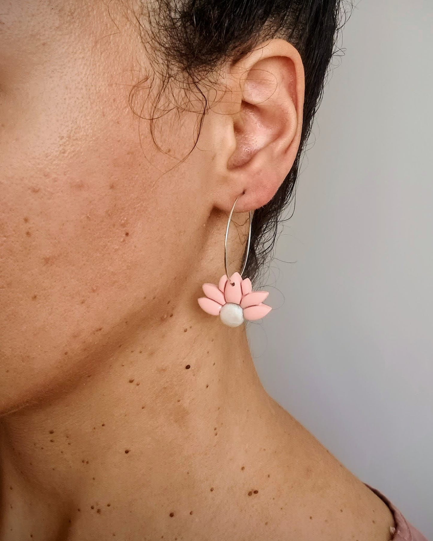 Close-up of a person wearing a floral hoop earring with a pearl centre.