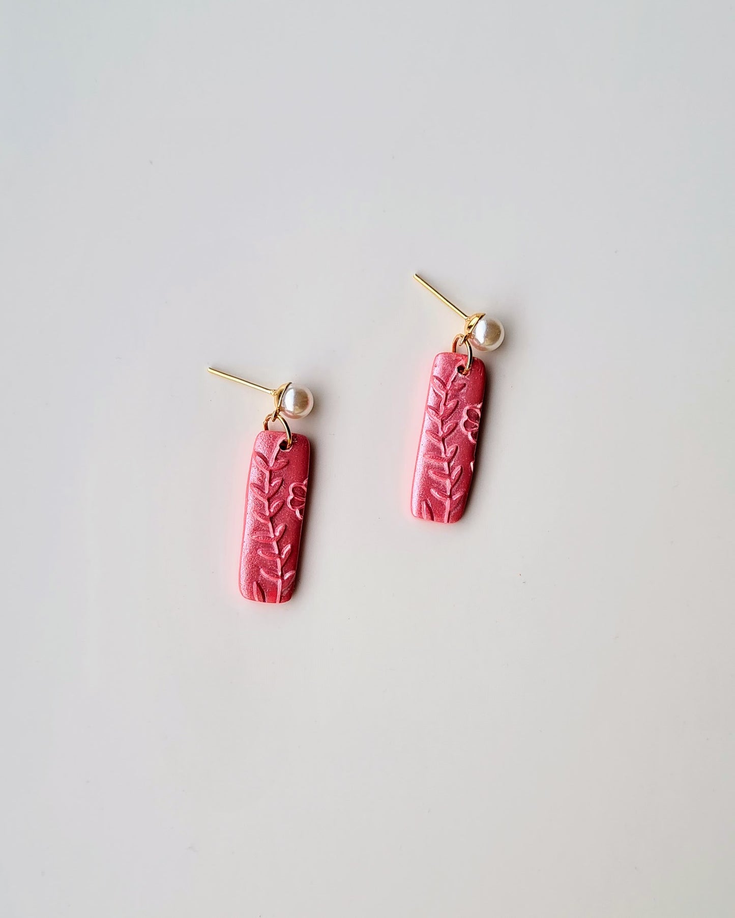 Shimmery pink earrings with leaf pattern and pearl pendant on a light grey background
