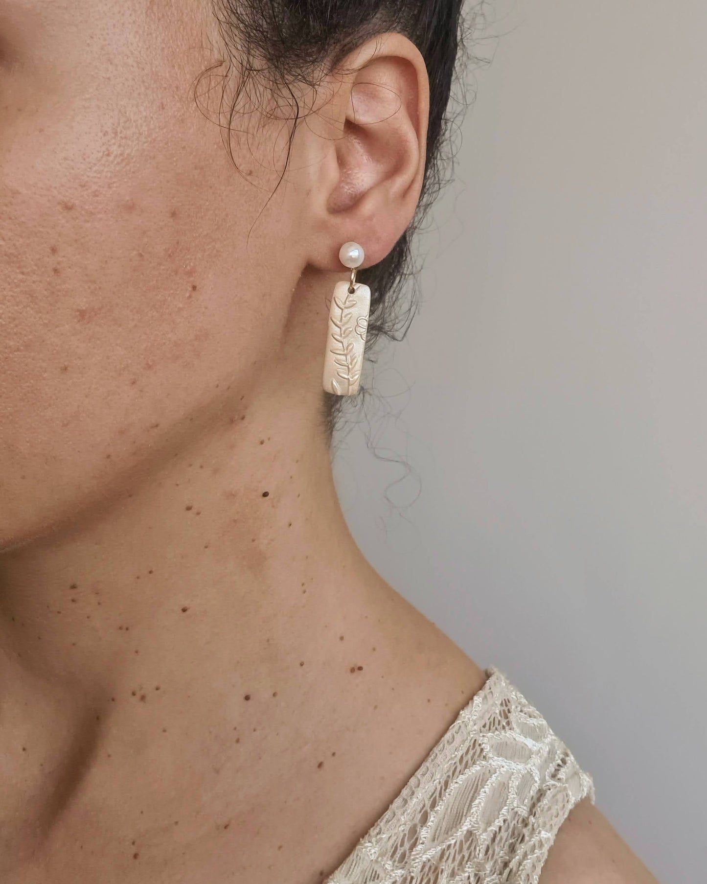 Close-up of a person wearing a shimmery yellow earrings and with accents on a neutral background