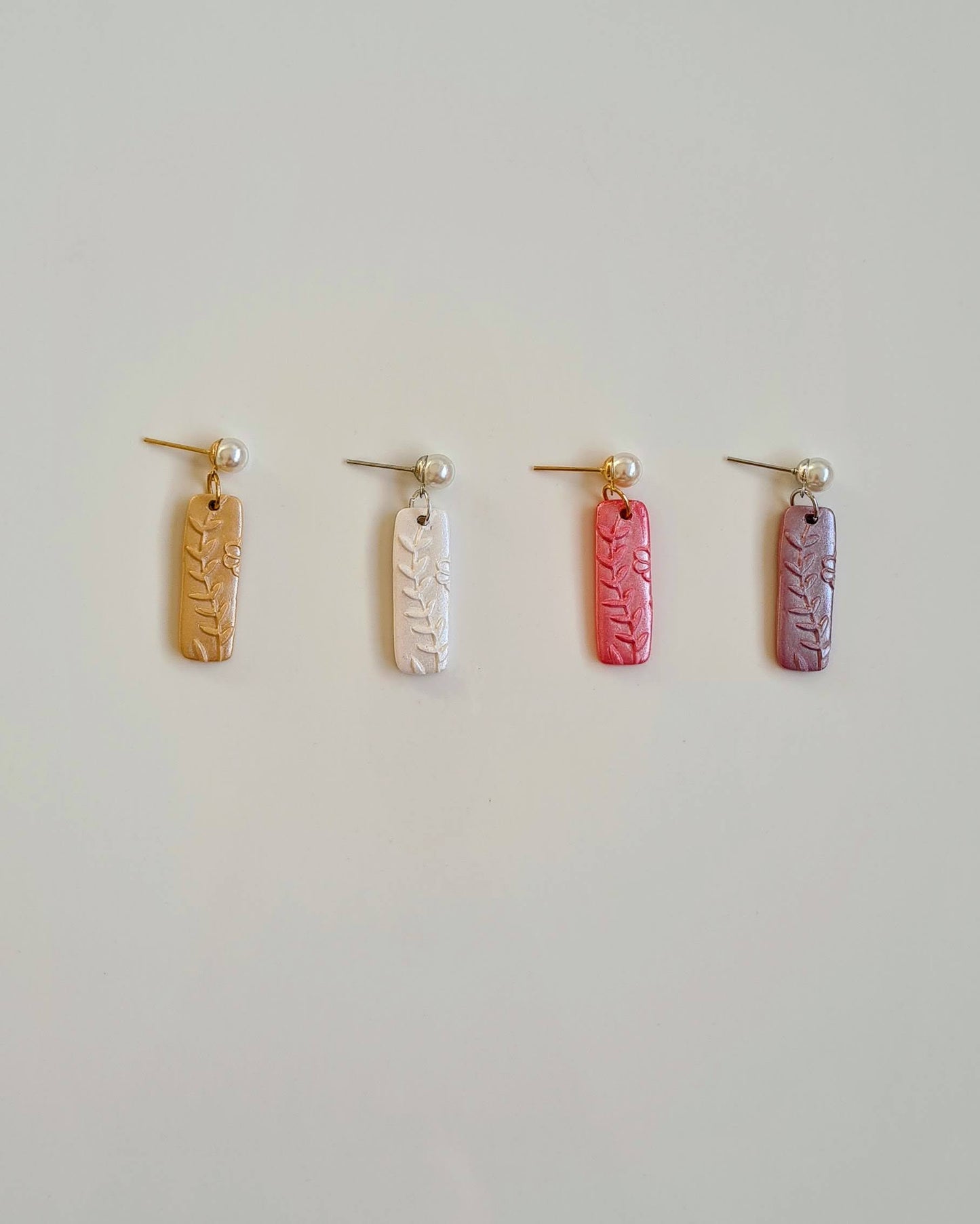 Four pairs of earrings in different colors on a light grey background