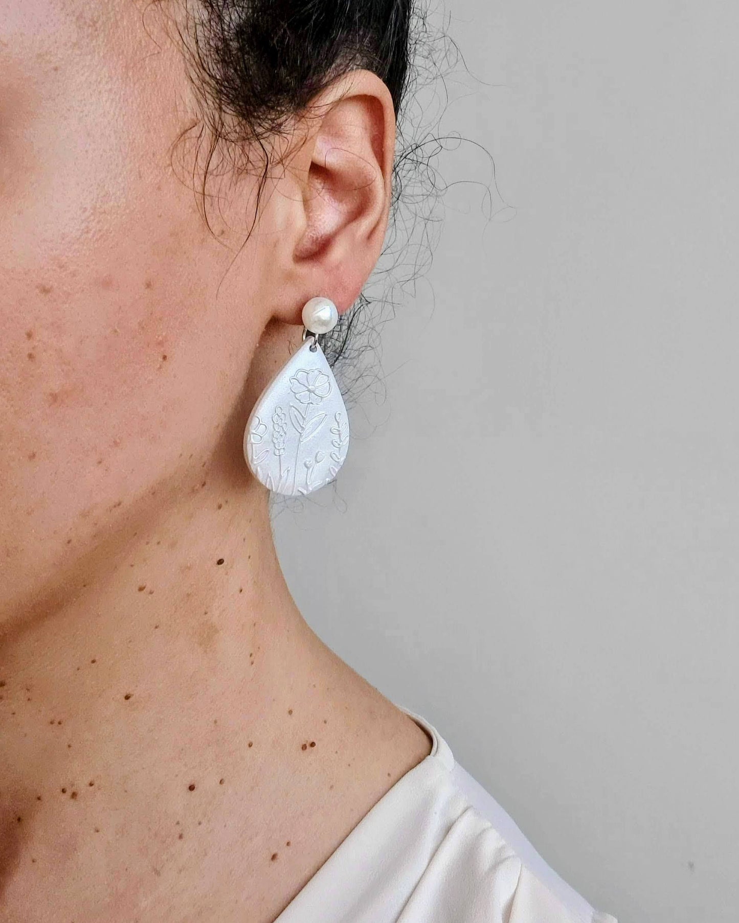 Close-up of a person wearing a white teardrop earring against a neutral background