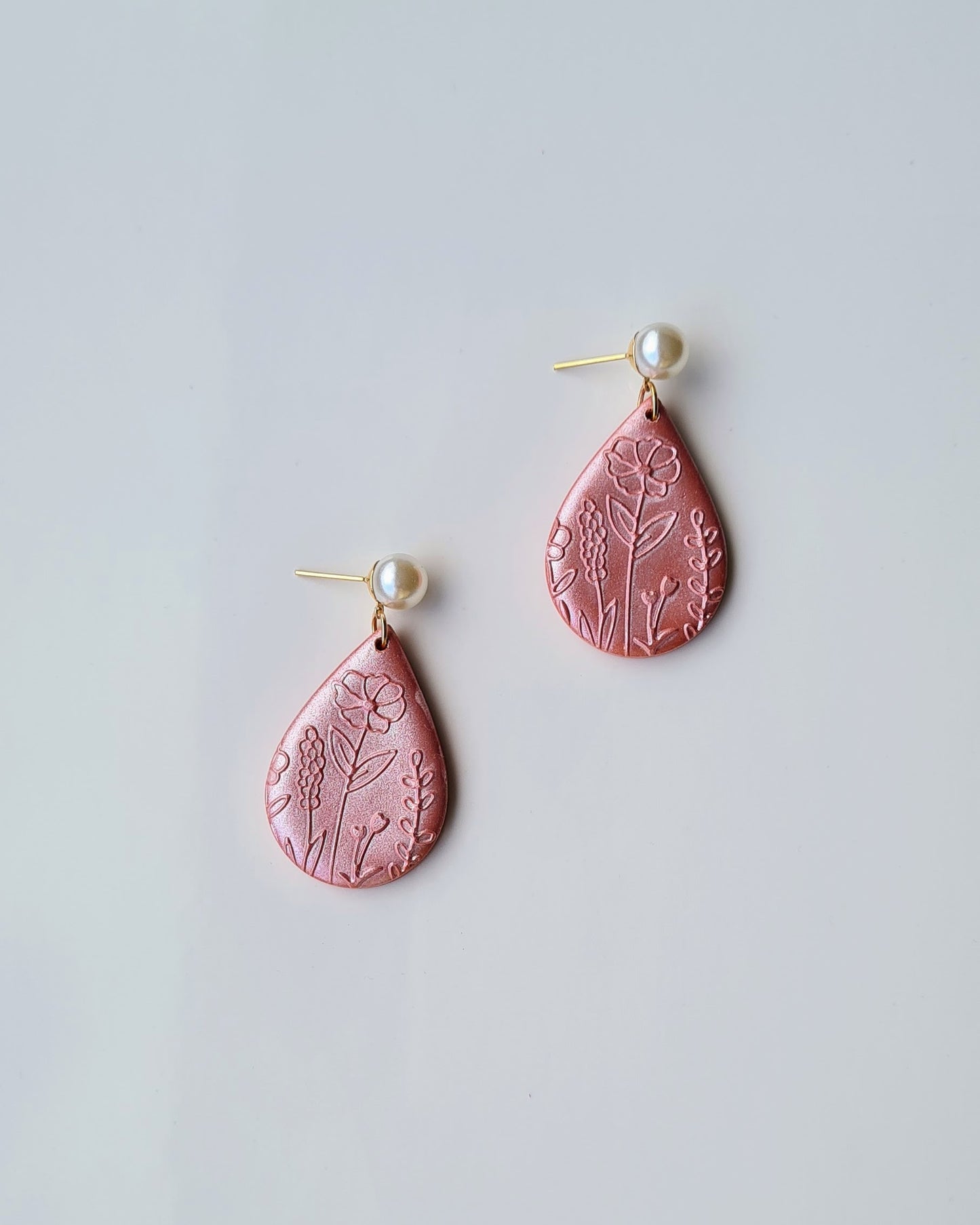 Pair of orange teardrop earrings with floral patterns and shimmery finish on a light grey background