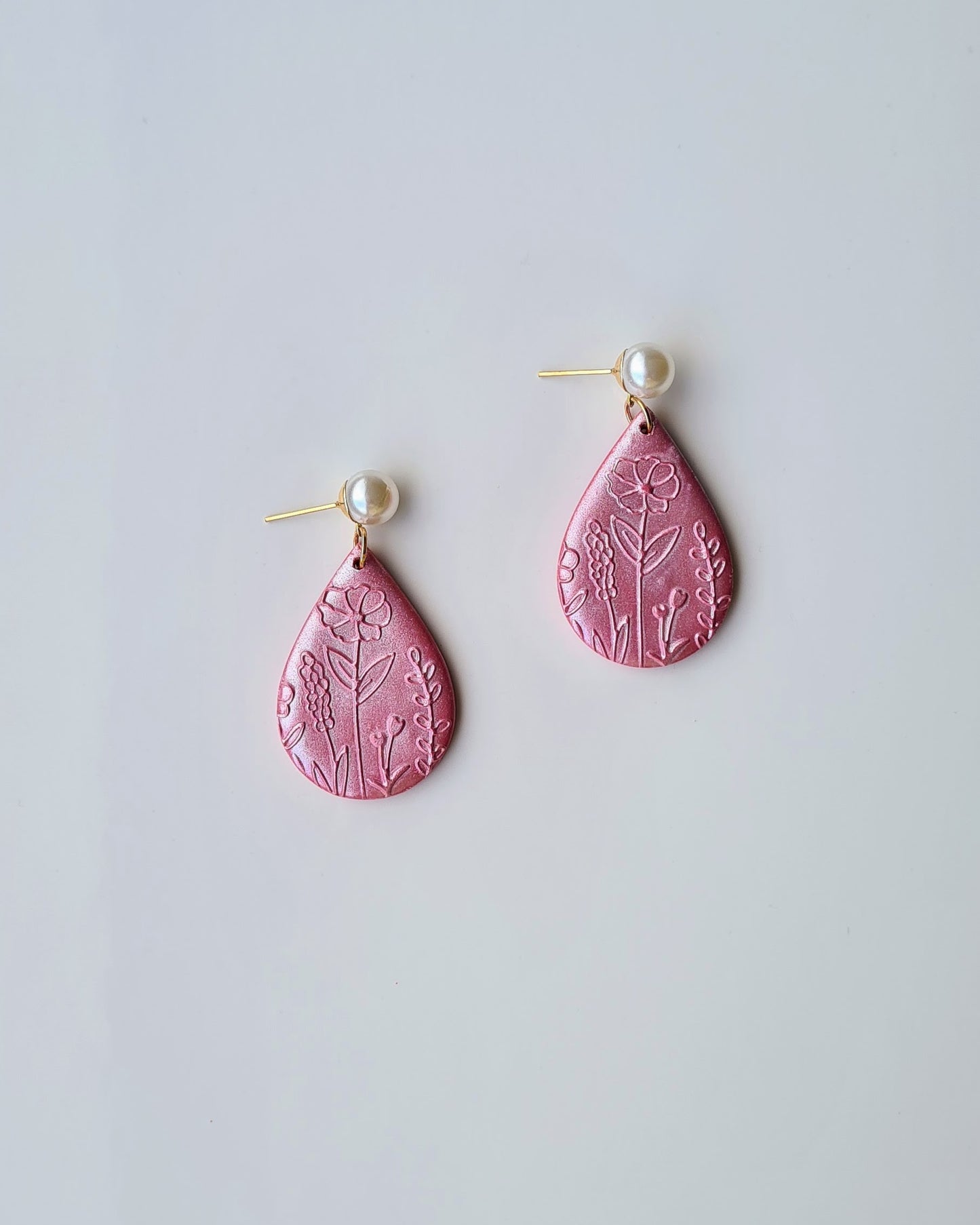 Pink teardrop earrings with floral patterns and pearlescent finish on a light grey background.