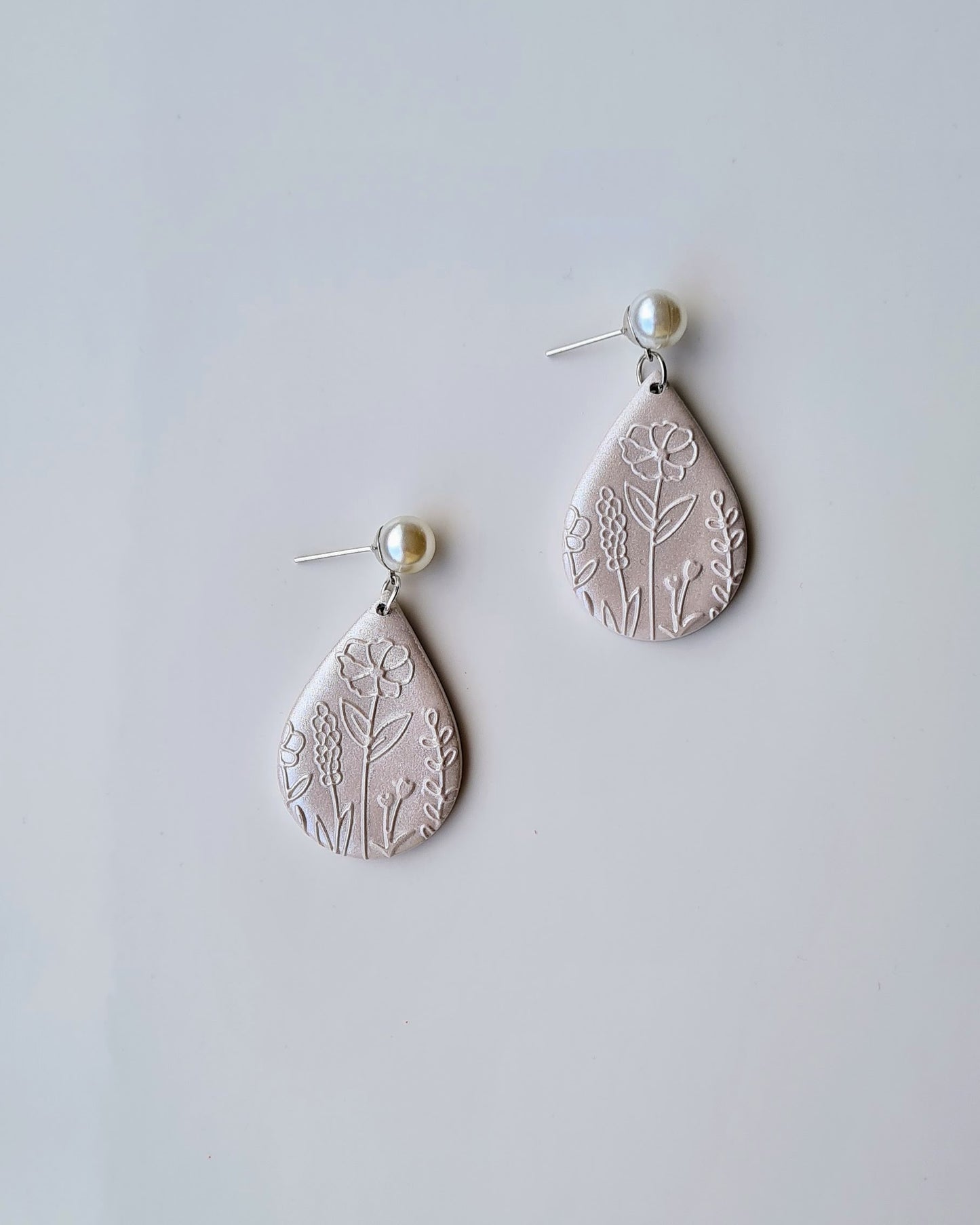 Teardrop-shaped earrings with floral patterns and a shimmery finish on a light grey background