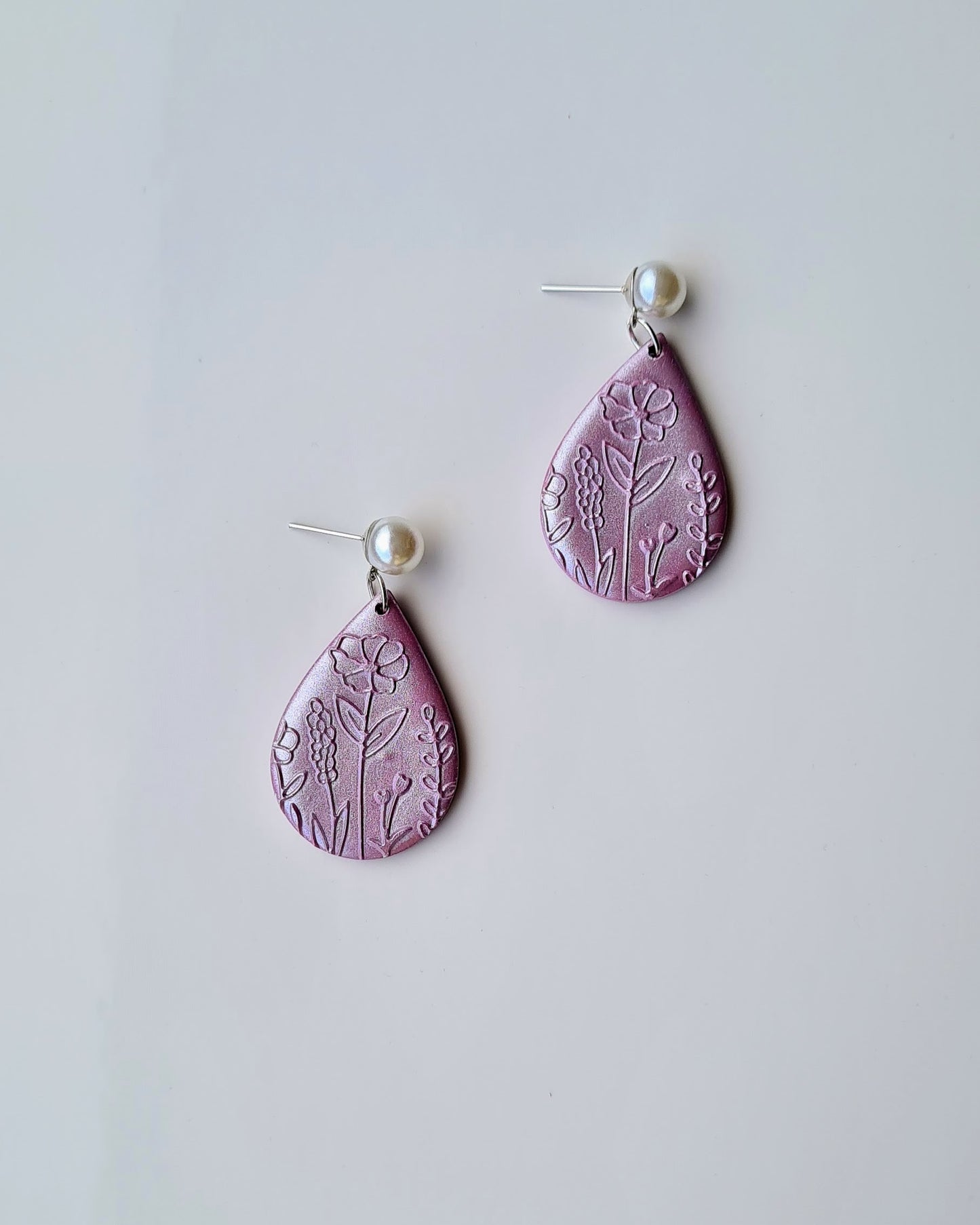 Pair of lilac teardrop earrings with floral patterns and pearlescent finish on a light grey background