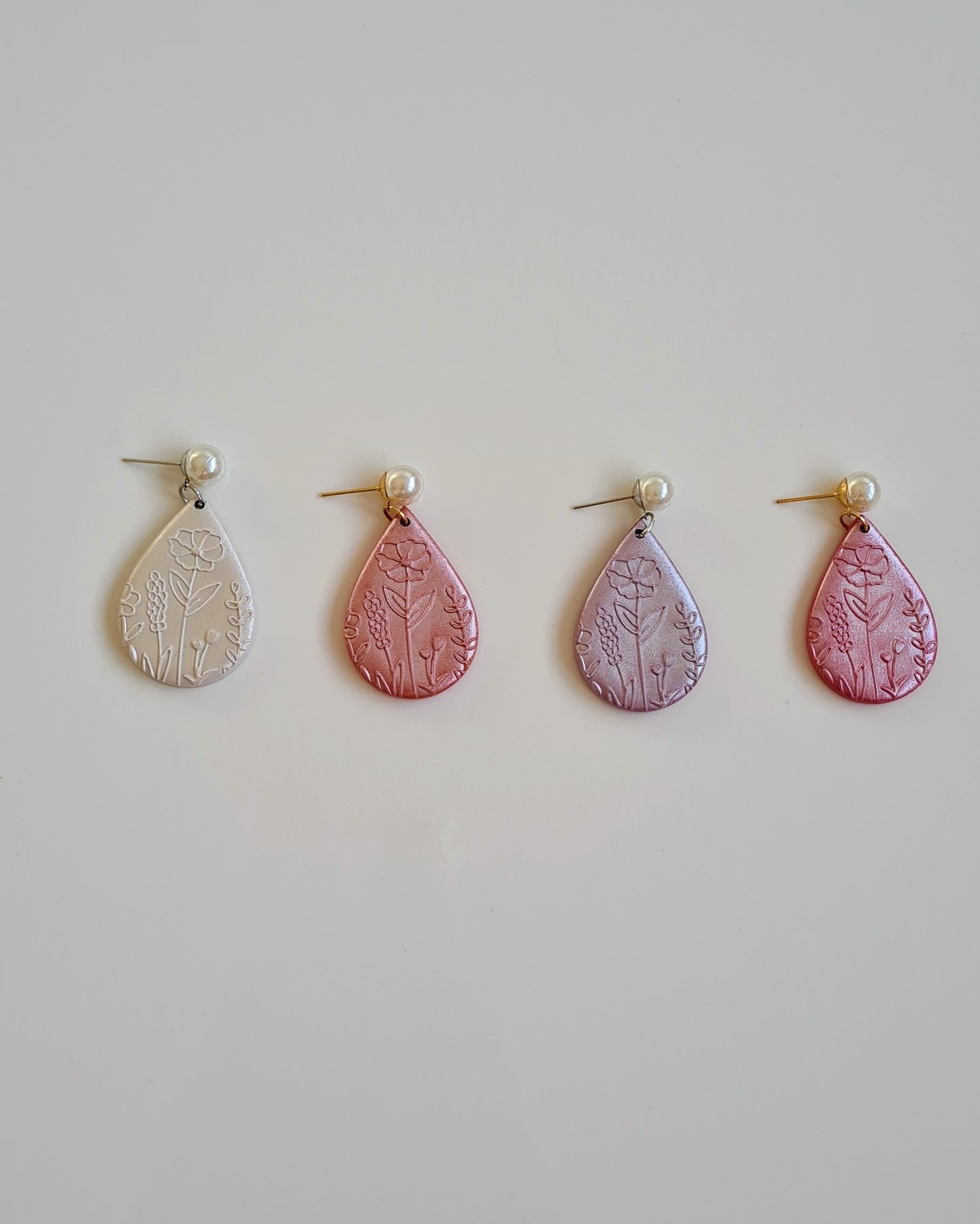 Four pairs of drop earrings with floral patterns on a light grey background