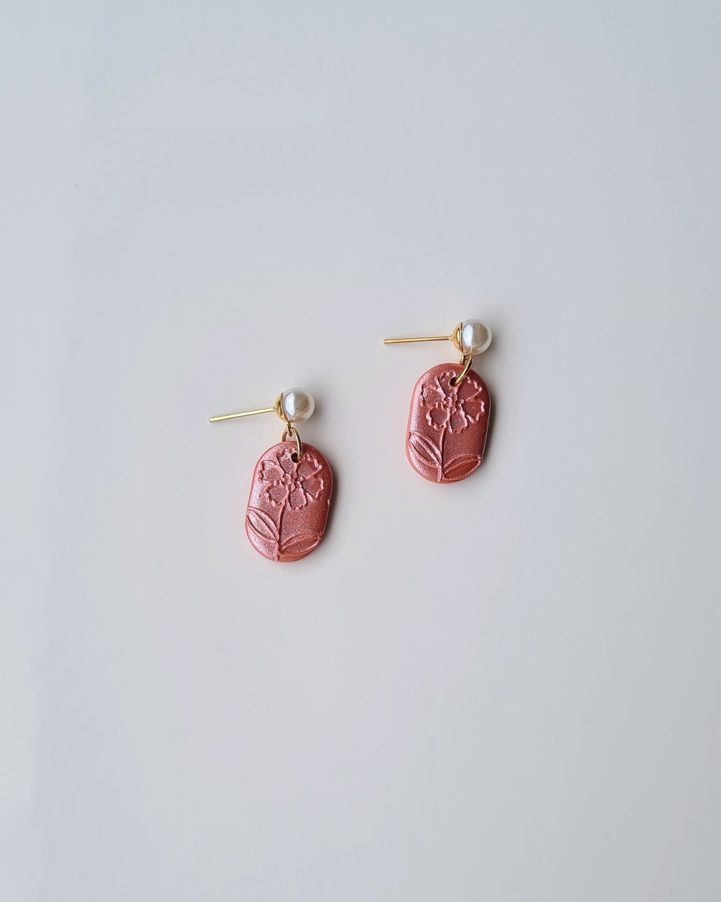 Pair of orange earrings with floral texture and pearl accent on a light grey background