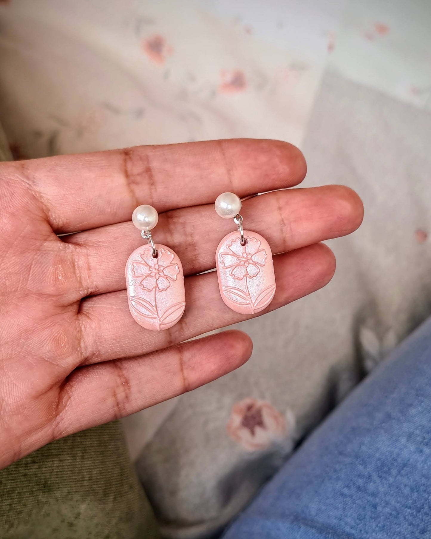 Hand holding two pink earrings with a floral patterned background