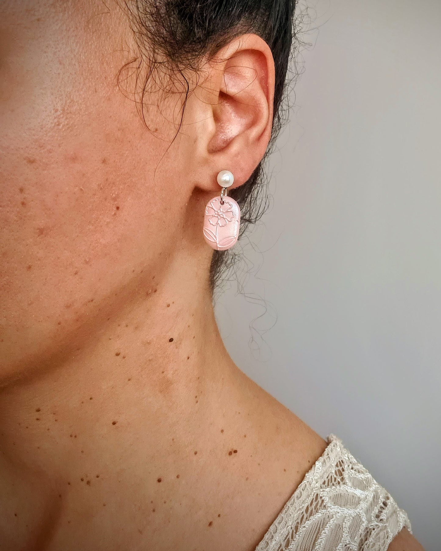 Close-up of a person wearing shimmery coral earrings with a neutral background