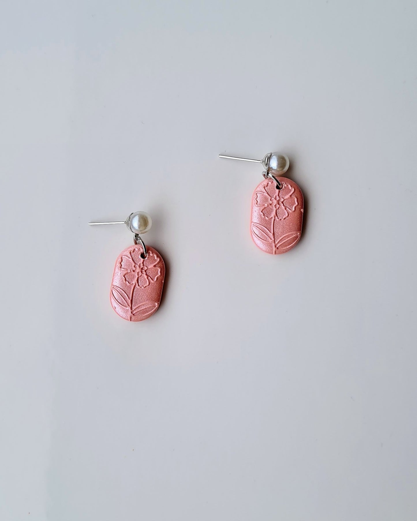 Pair of pink earrings with floral design on a light gray background