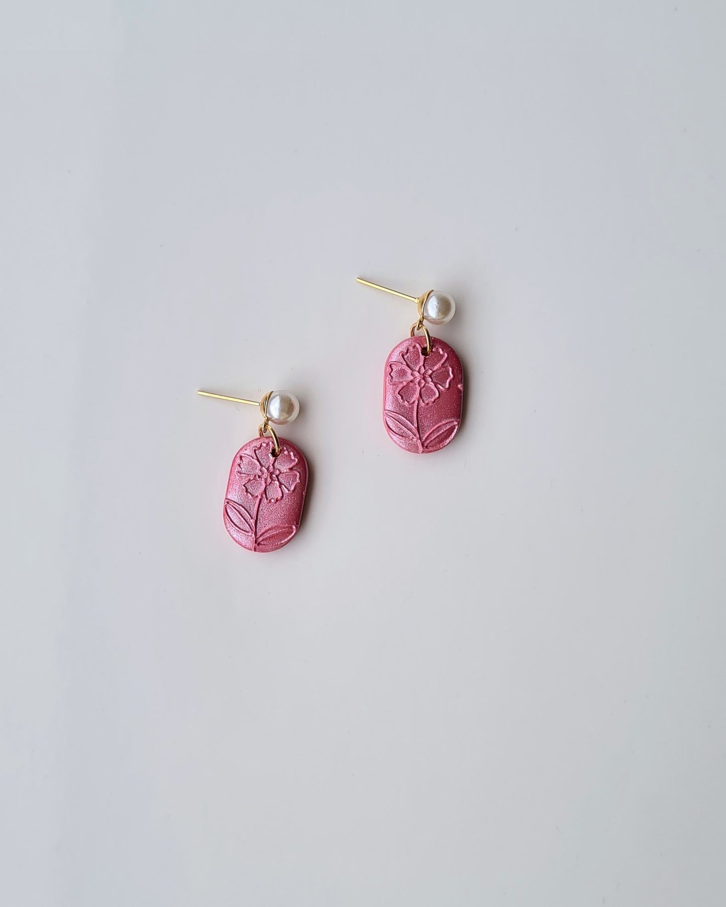 Pair of pink earrings with floral pattern and pearl accent on a light grey background