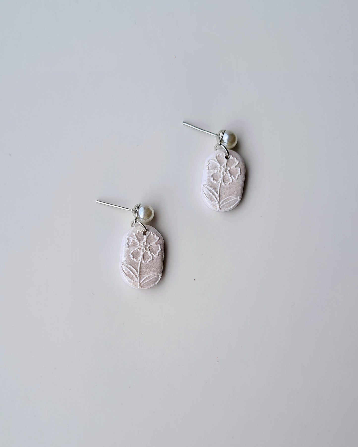 Pair of white earrings with floral texture and pearl accent on a light grey background
