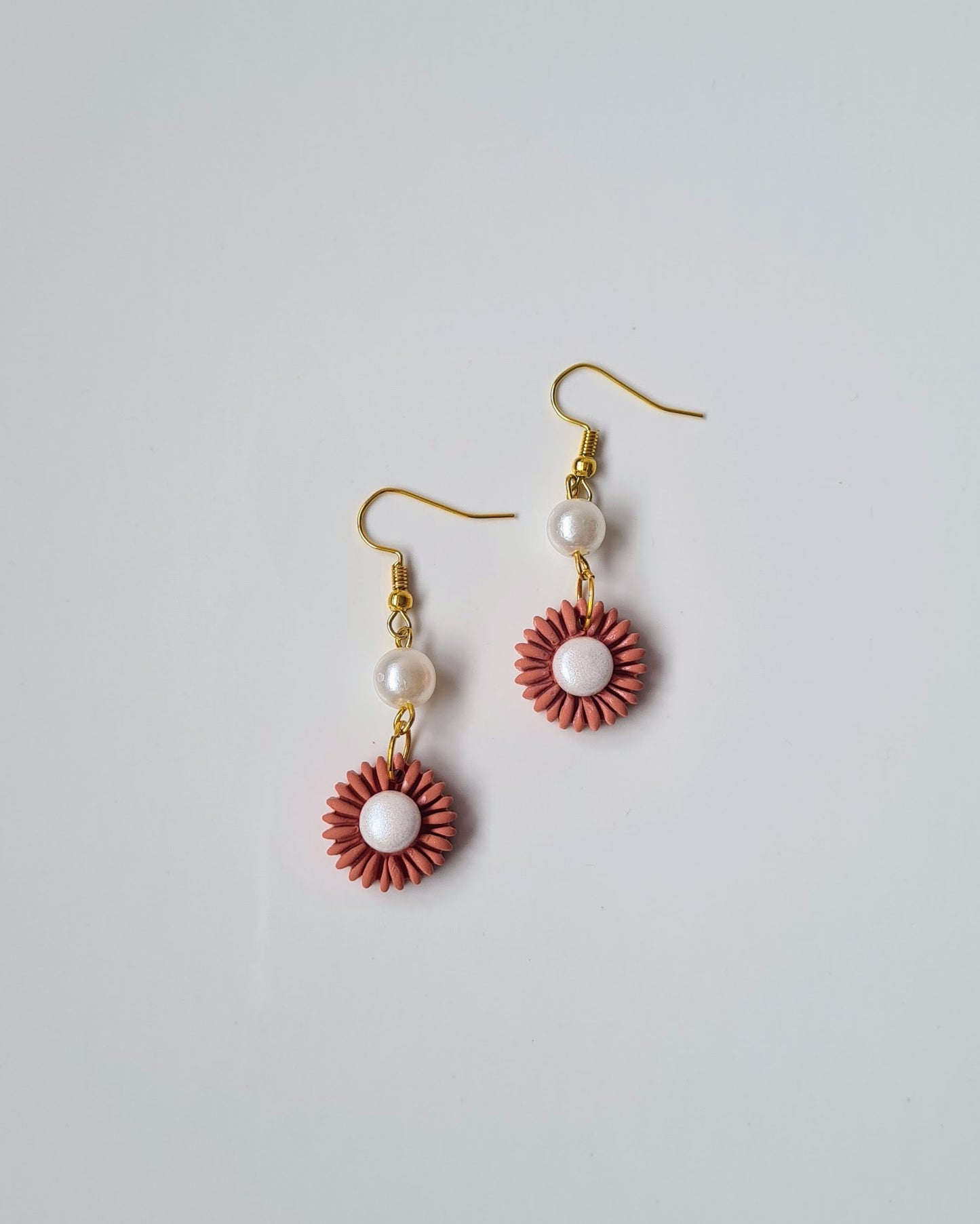 Pair of earrings with pink floral designs and pearl beads on a light gray background