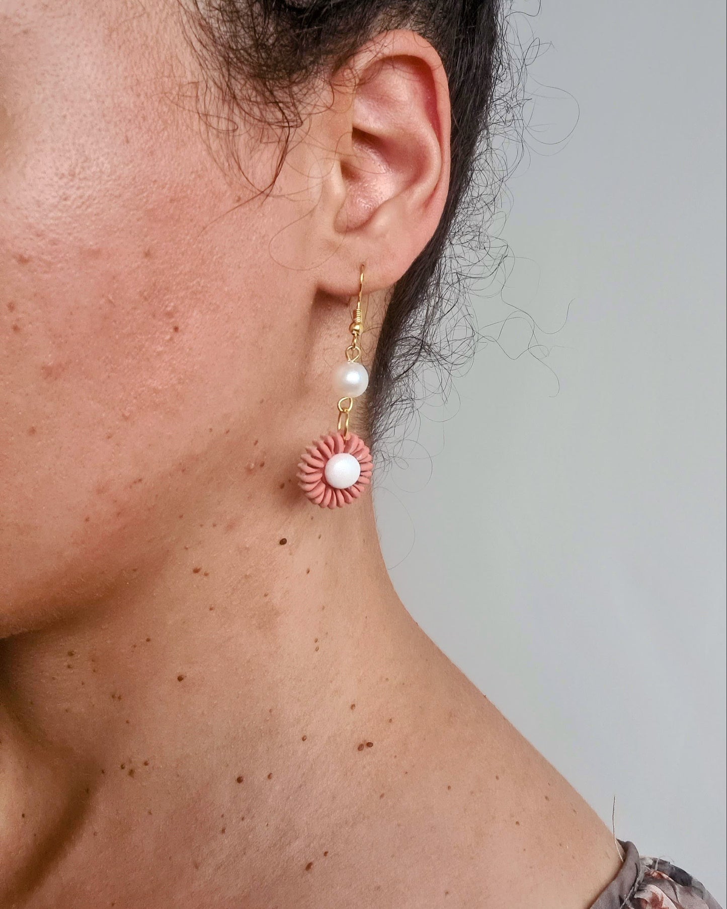 Close-up of a person wearing a floral earring with a pearl center.