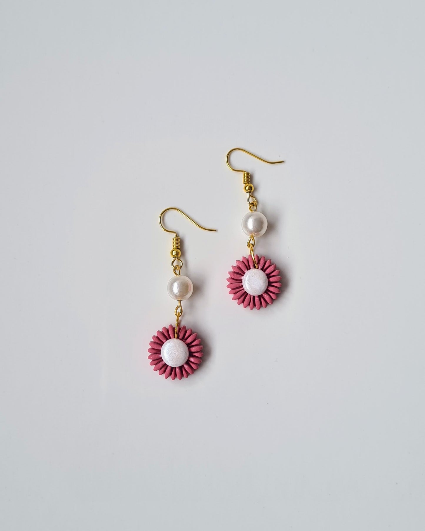 Pair of earrings with pink floral designs and pearl beads on a light gray background