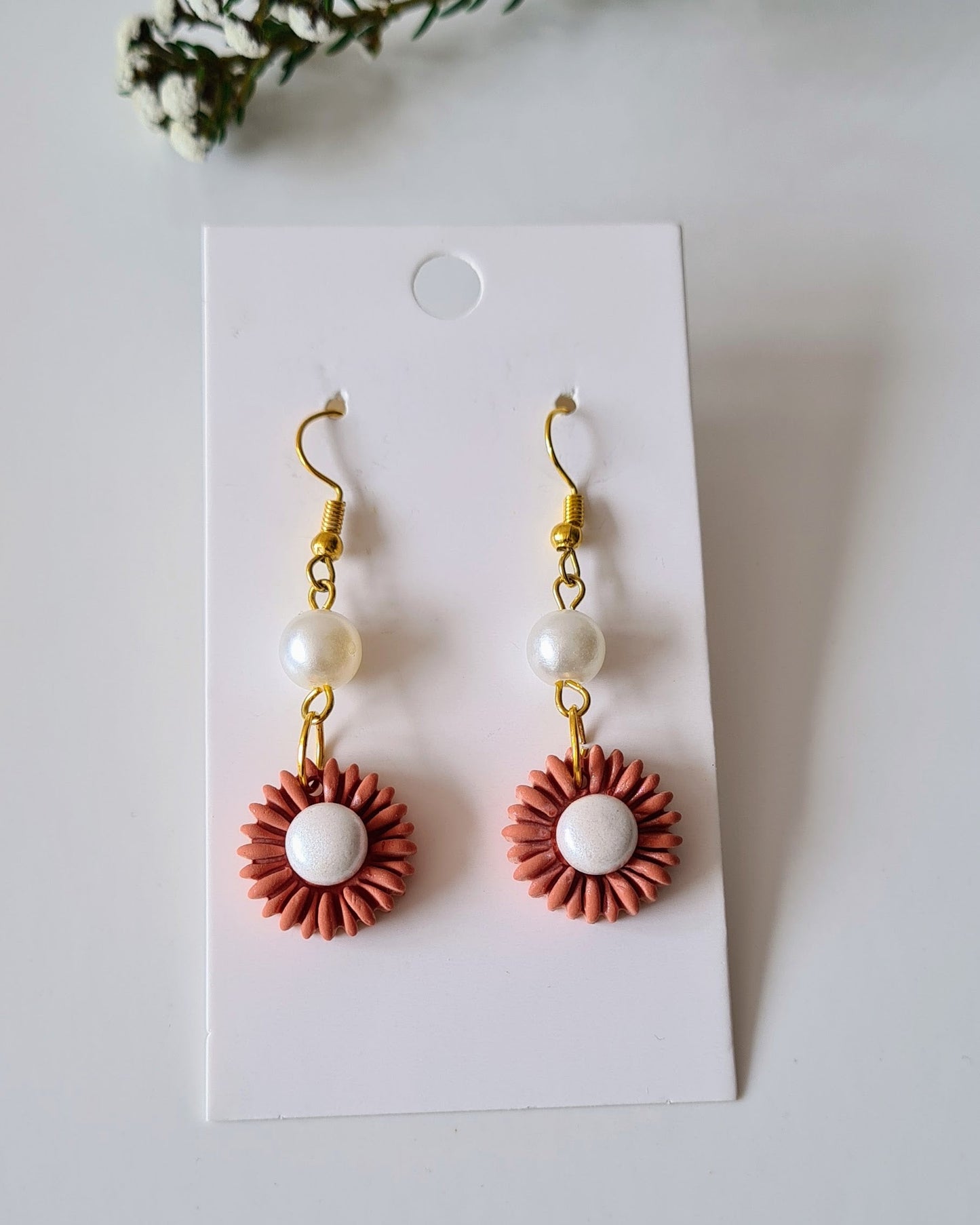 Pair of drop earrings on a white card with greenery around