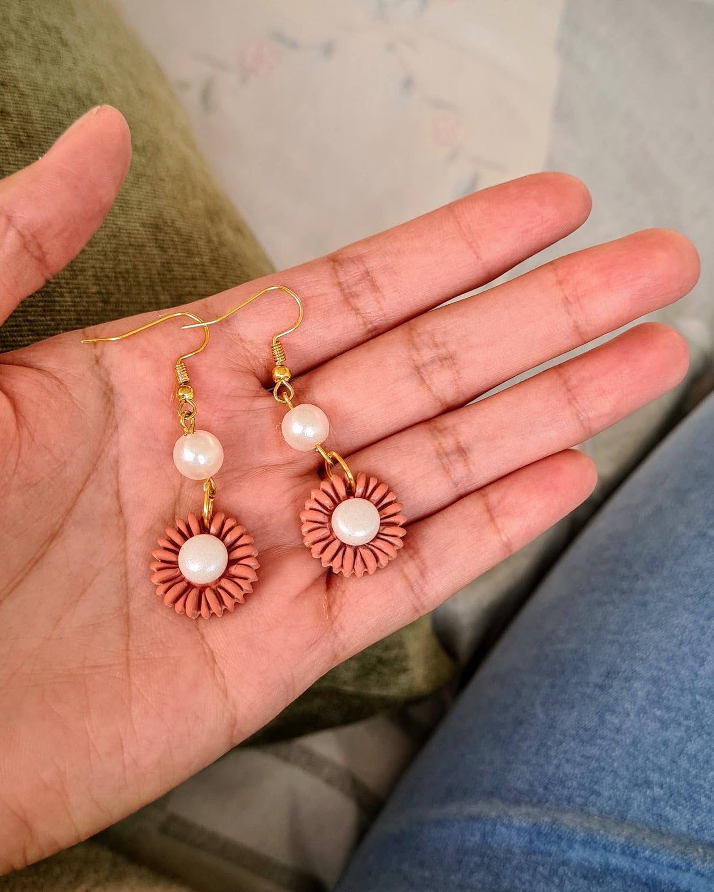 Hand holding two pairs of earrings against a neutral background