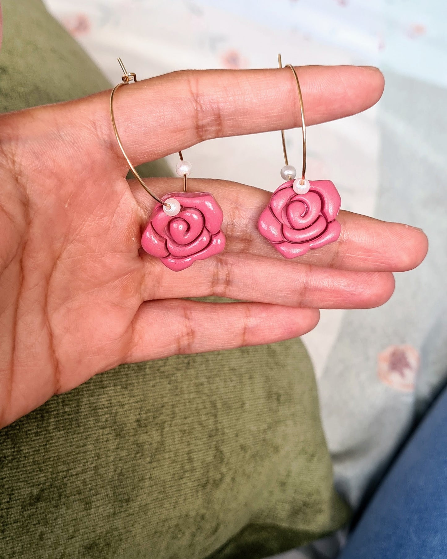 Hand holding rose-shaped earrings against a floral background