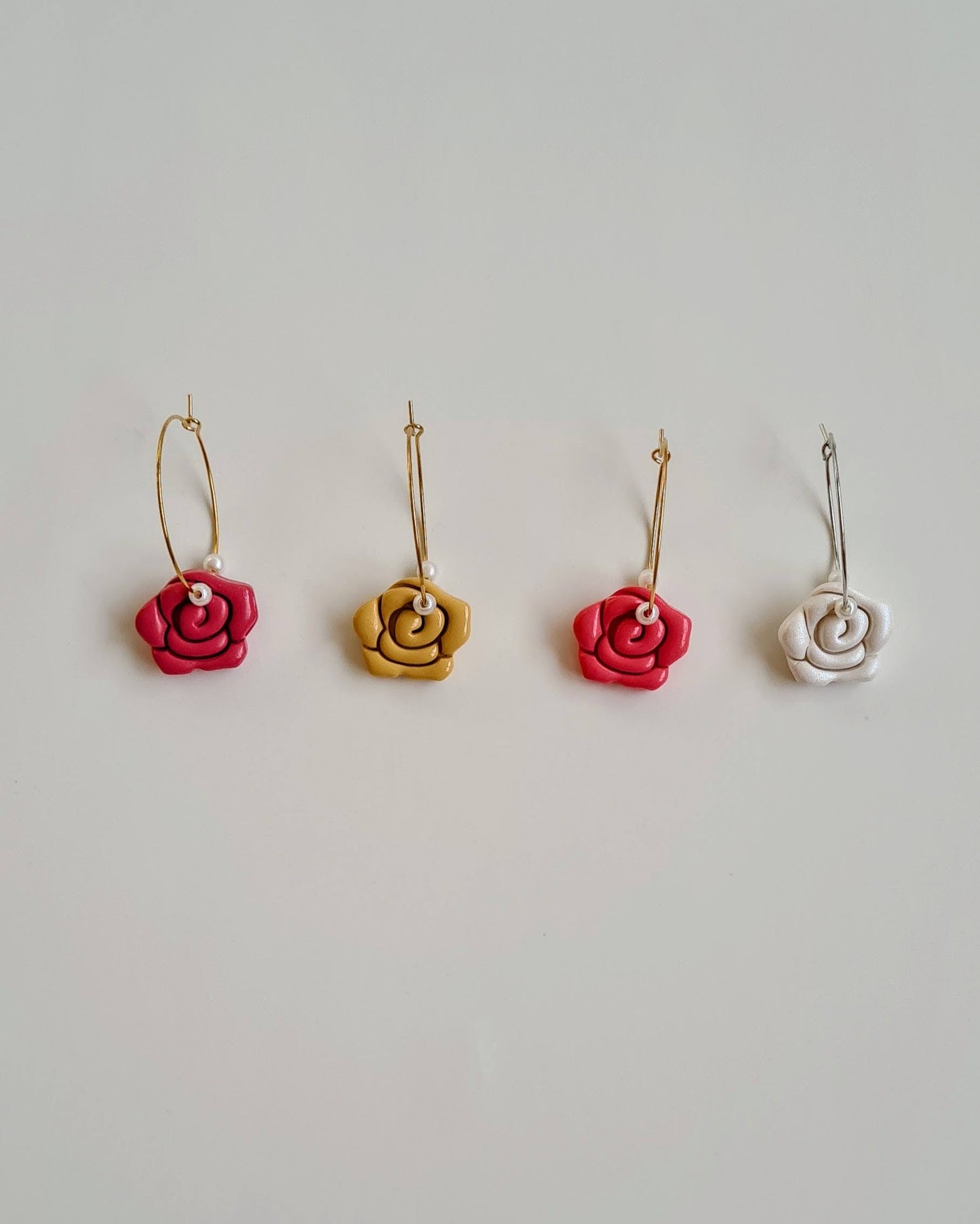 Four pairs of rose-shaped earrings in different colors on a light gray background