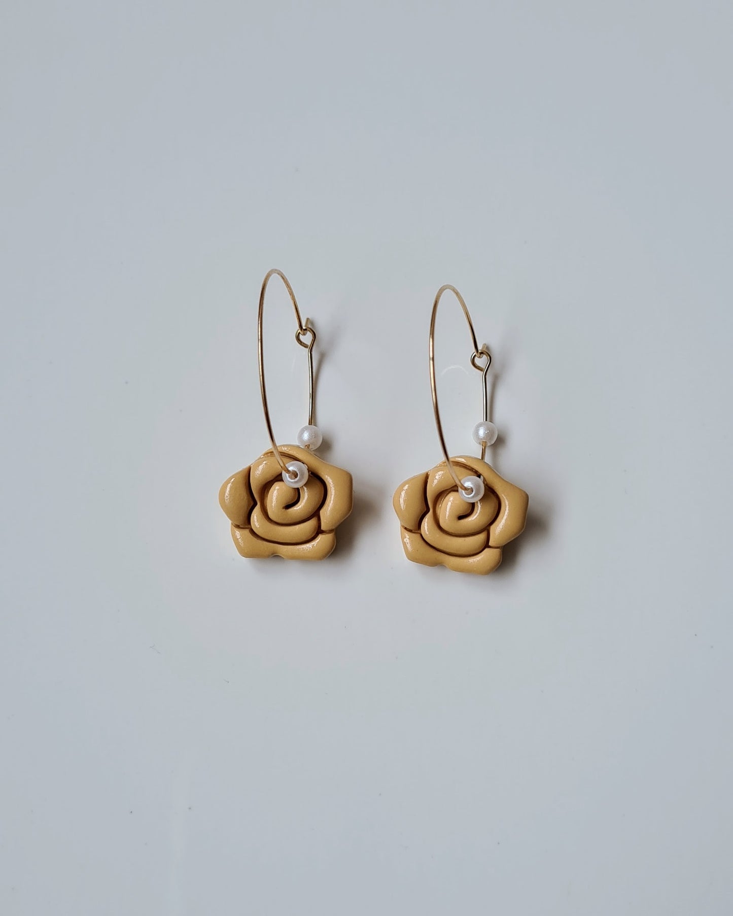 Pair of yellow rose-shaped earrings with pearl accents on a light grey background