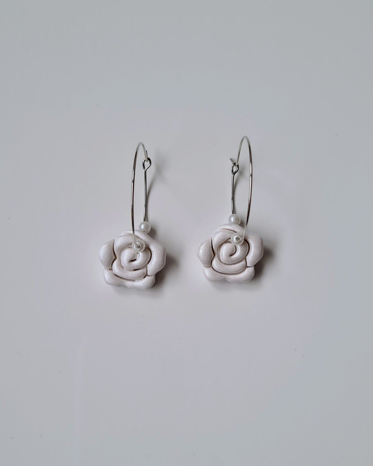 White rose-shaped hoop earrings on a light grey background