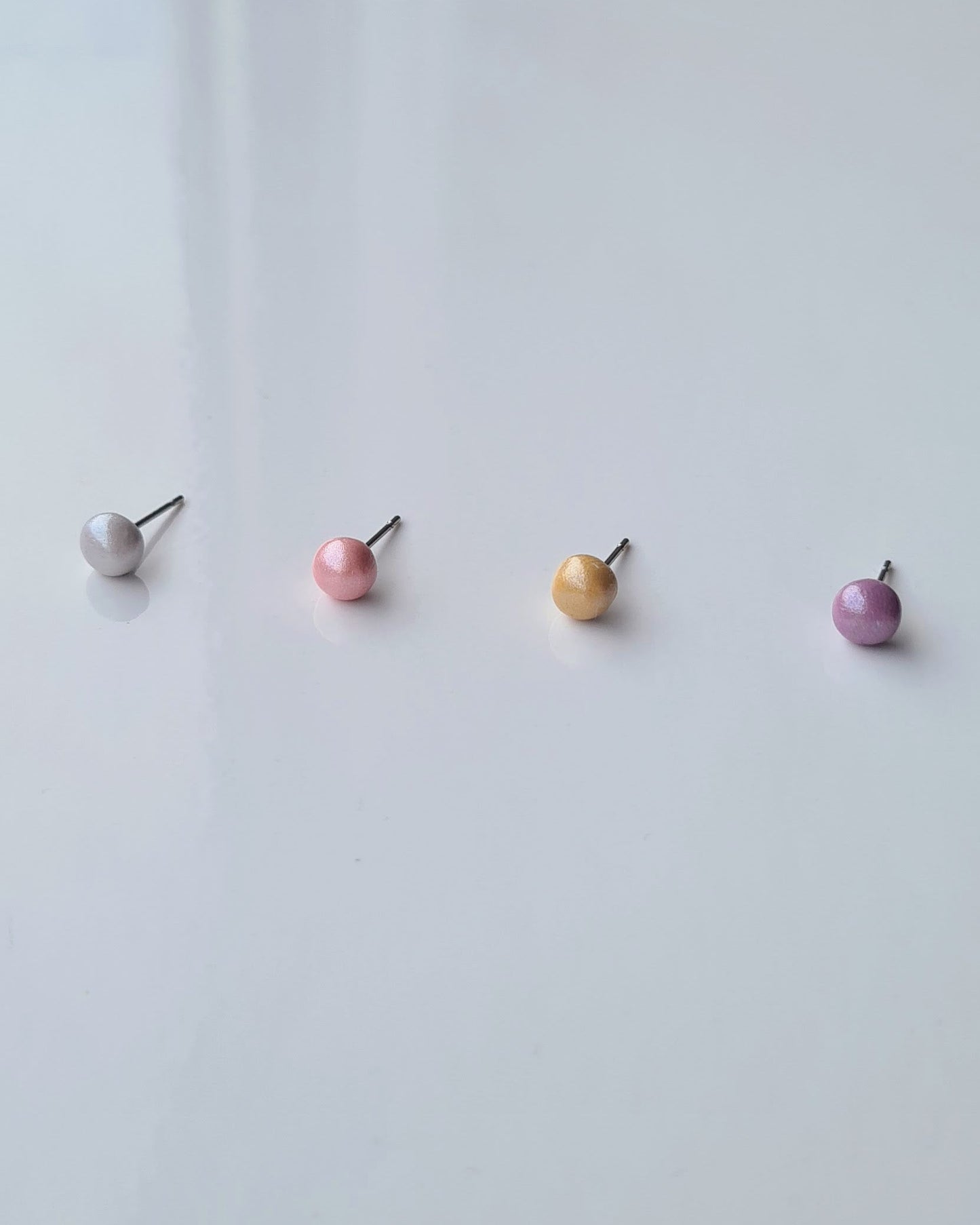 Four pearlescent studs in different colours on a light grey background