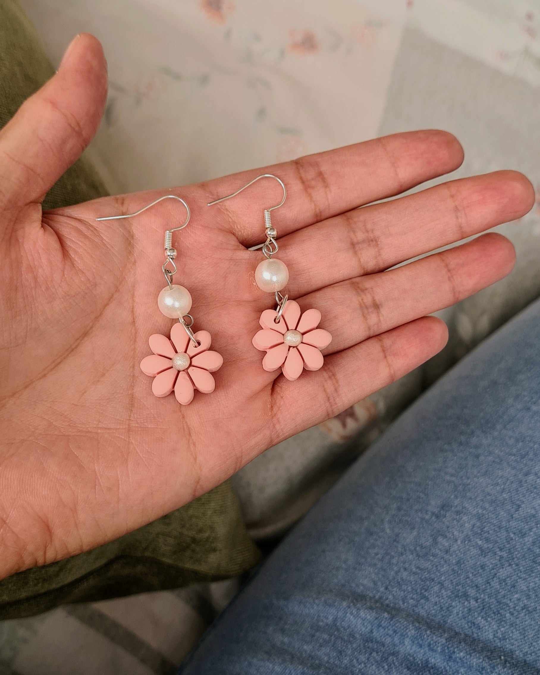 Hand holding pink flower earrings with a floral-patterned background