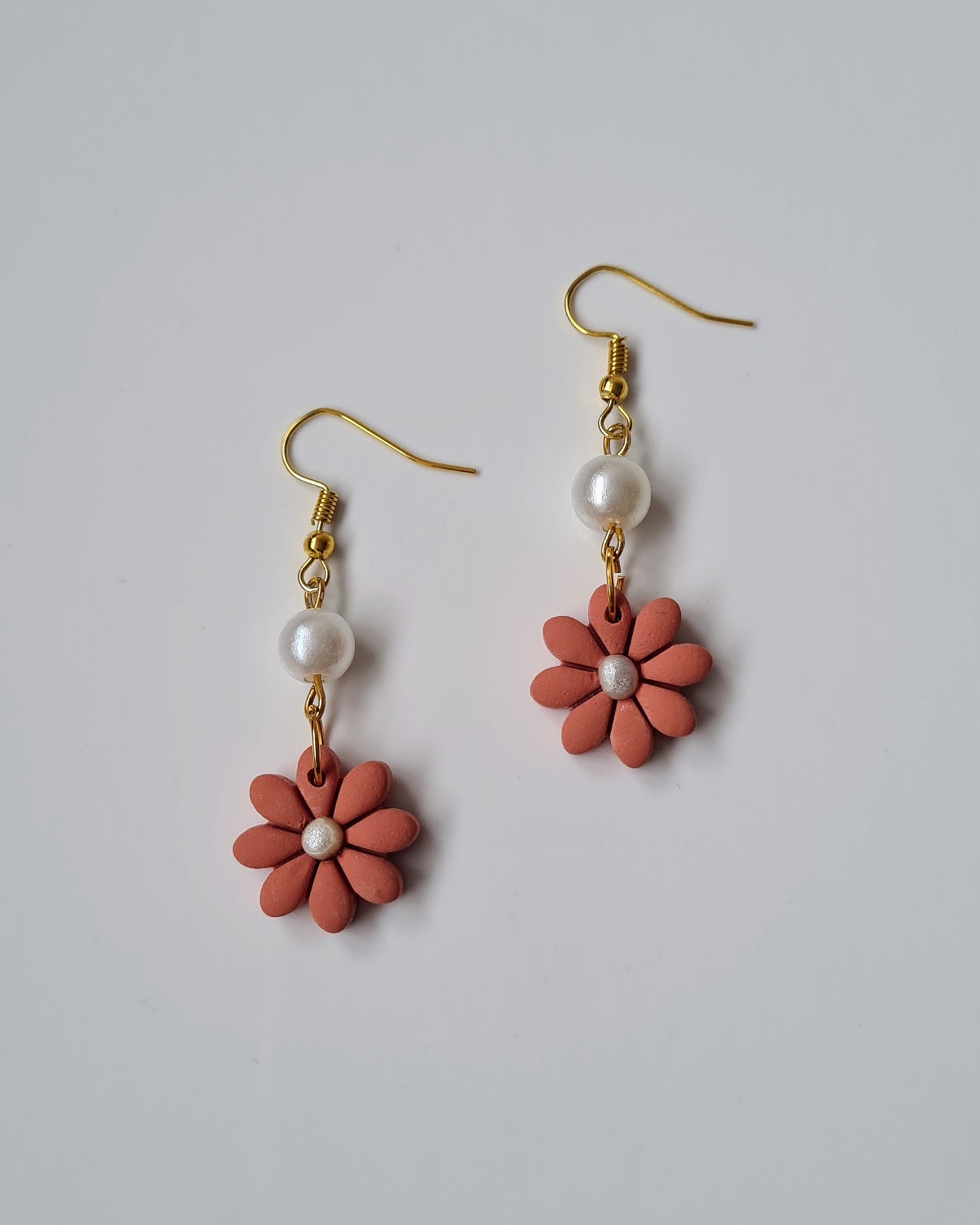 Pair of earrings with pink flower-shaped charms and pearl beads on a light gray background