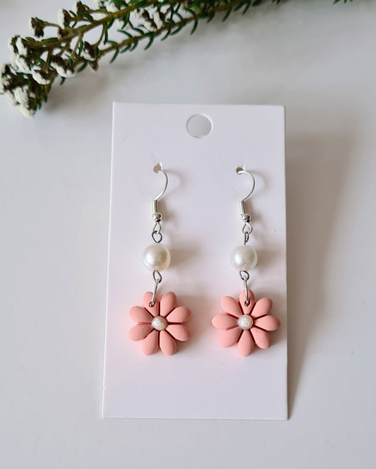 Pair of pink flower-shaped earrings on a white card with greenery around.