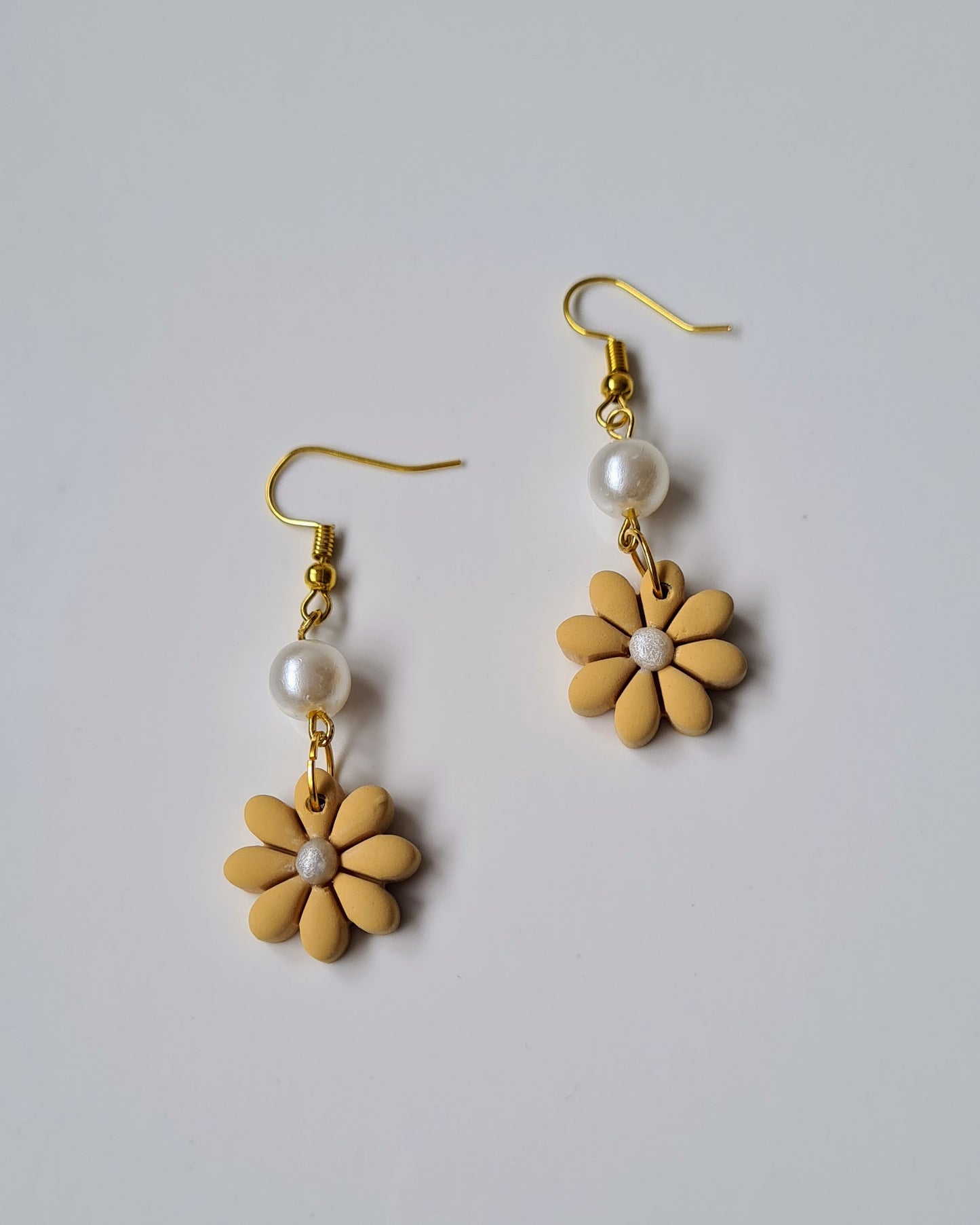 Pair of yellow flower-shaped earrings with pearl beads on a light gray background