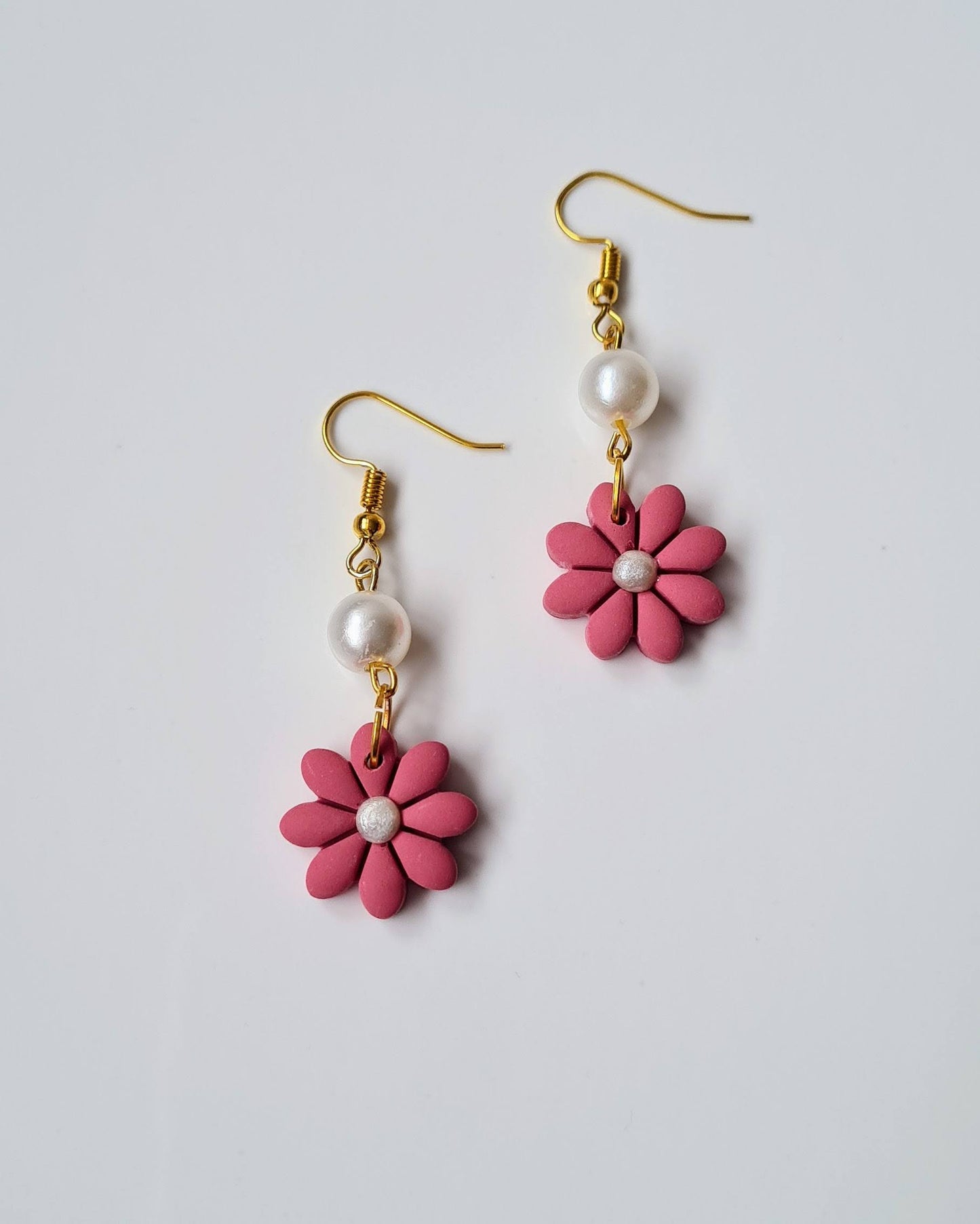 Pair of pink flower-shaped earrings with gold hooks and pearl centers on a light gray background