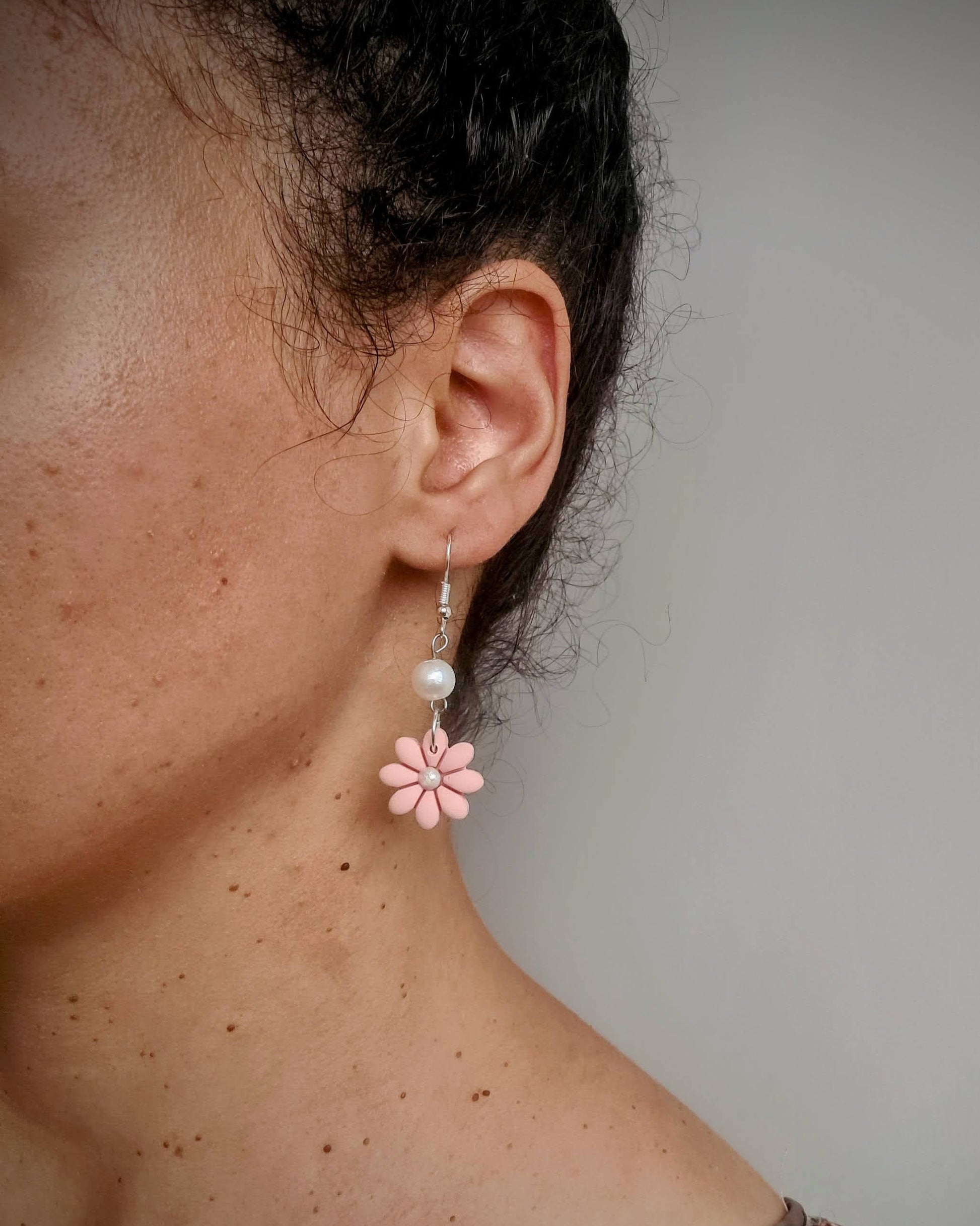 Close-up of a person wearing a pink flower earring with a plain background