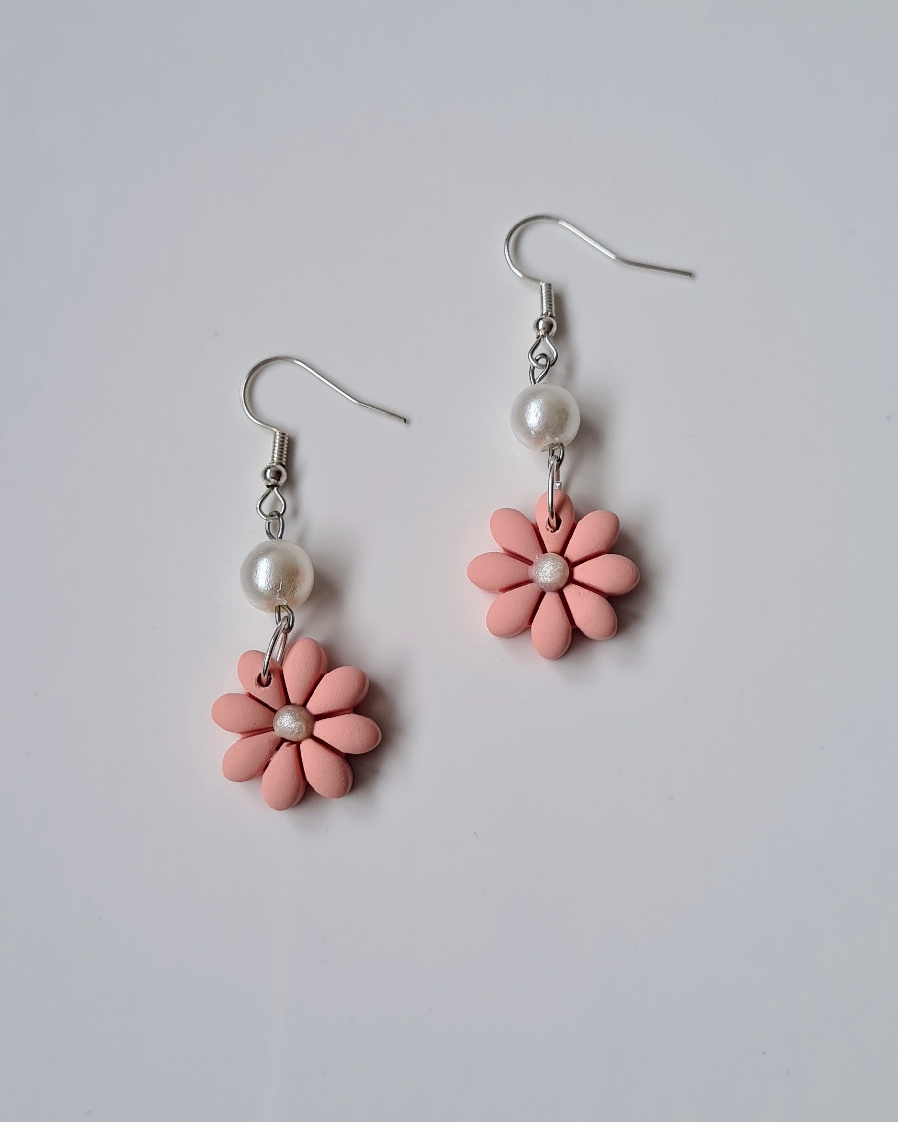 Pair of peac flower-shaped earrings with pearl accents on a light grey background