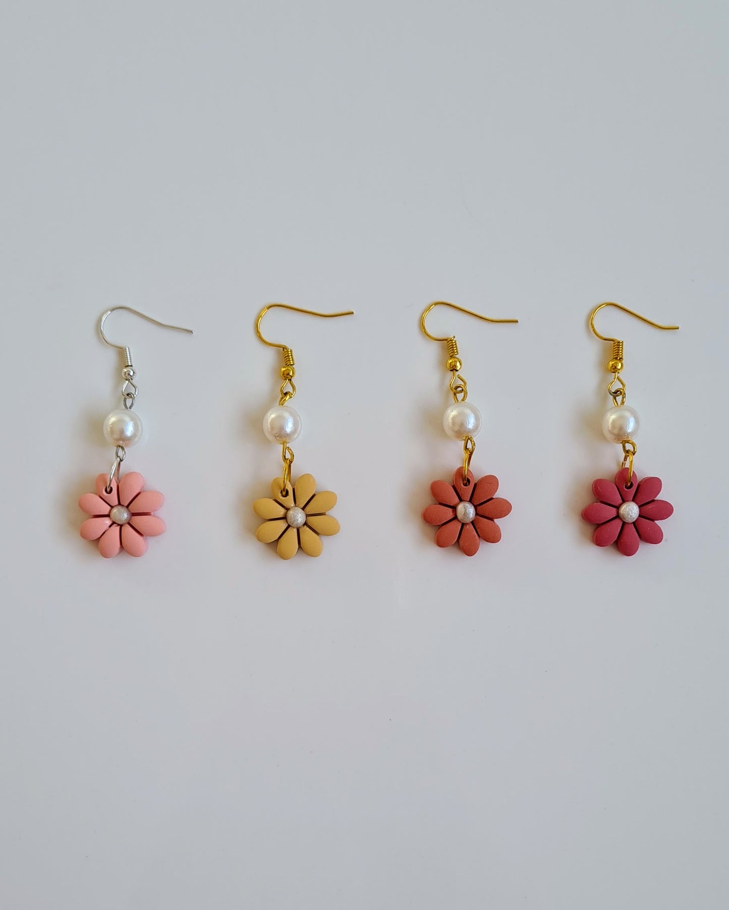 Set of four flower-shaped earrings with pink, yellow, orange and red flowers on a light grey background.